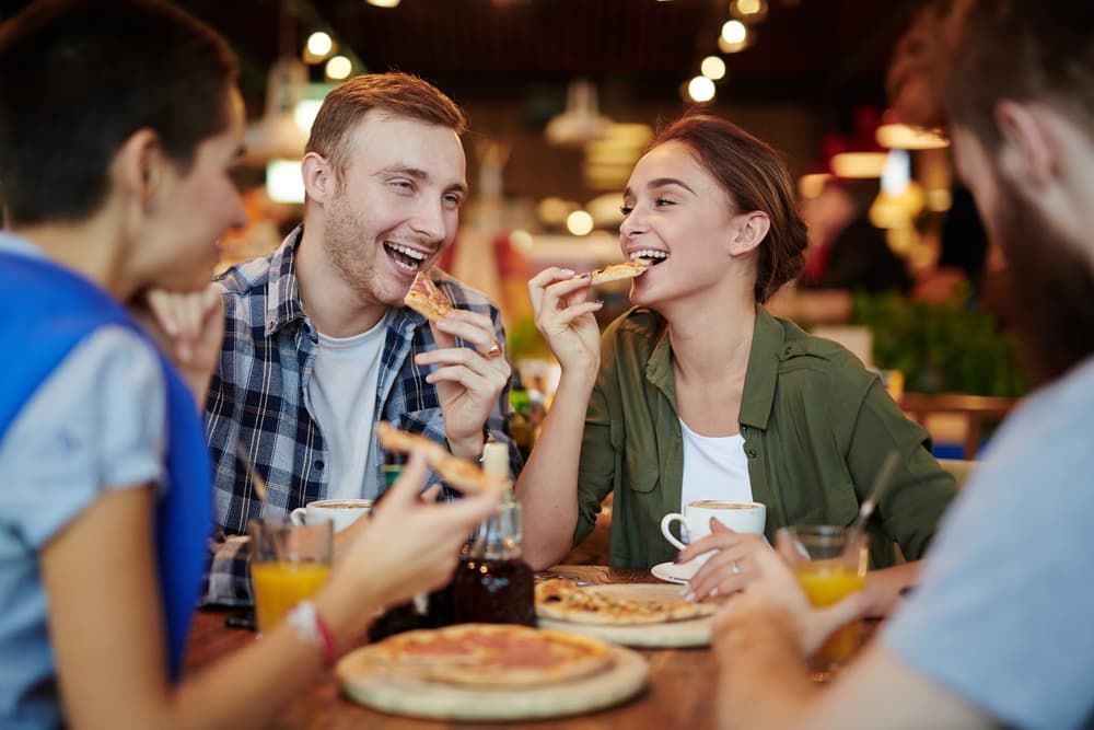 A Group of People Are Sitting at A Table Eating Pizza — Brews & Bites Beachside Cafe in Meikleville Hill, QLD