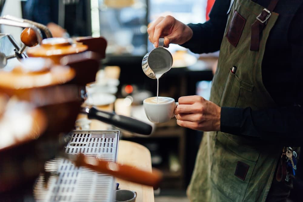A Barista Is Pouring Milk Into a Cup of Coffee — Brews & Bites Beachside Cafe in Meikleville Hill, QLD