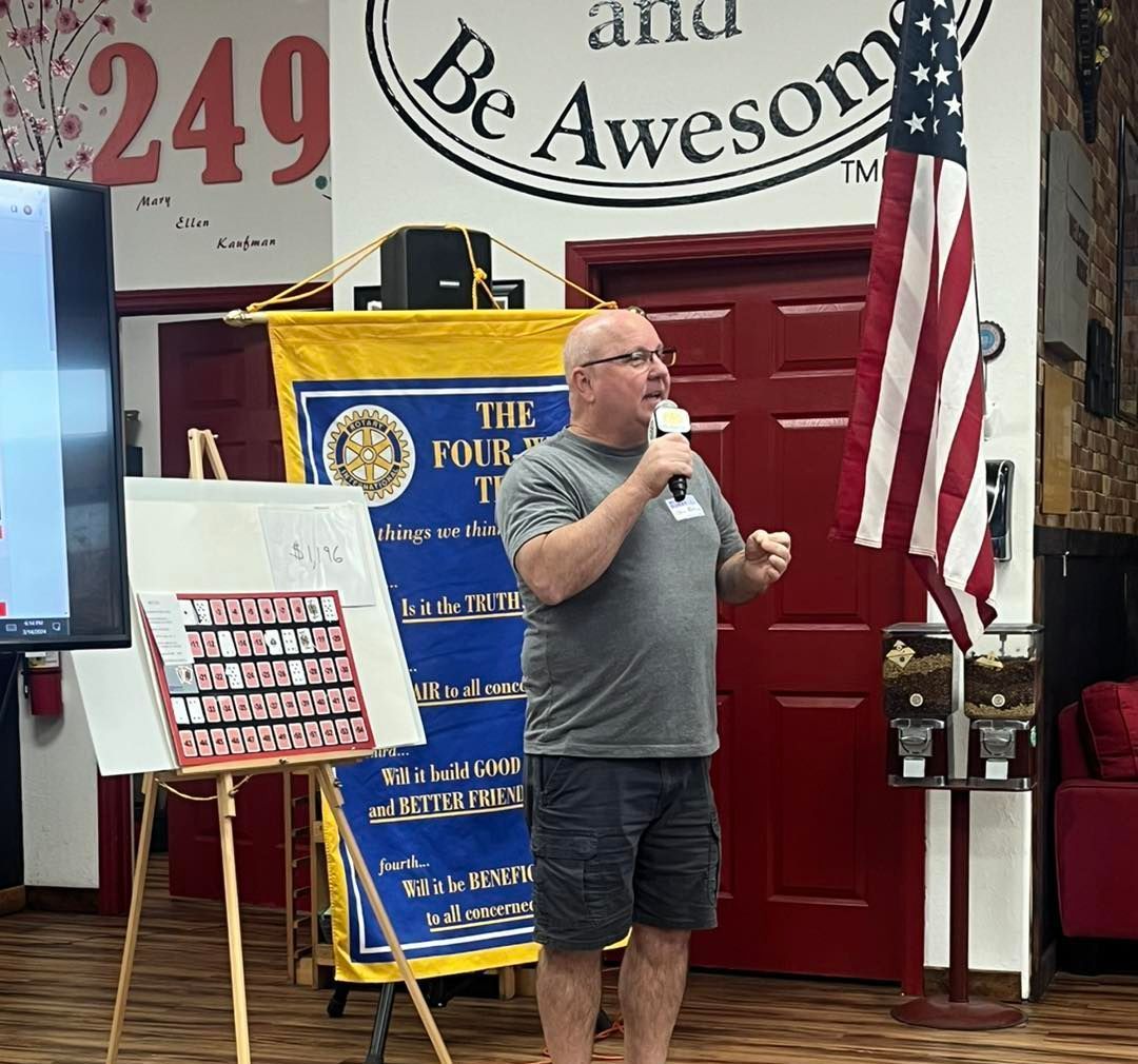 A man is speaking into a microphone in front of an american flag.