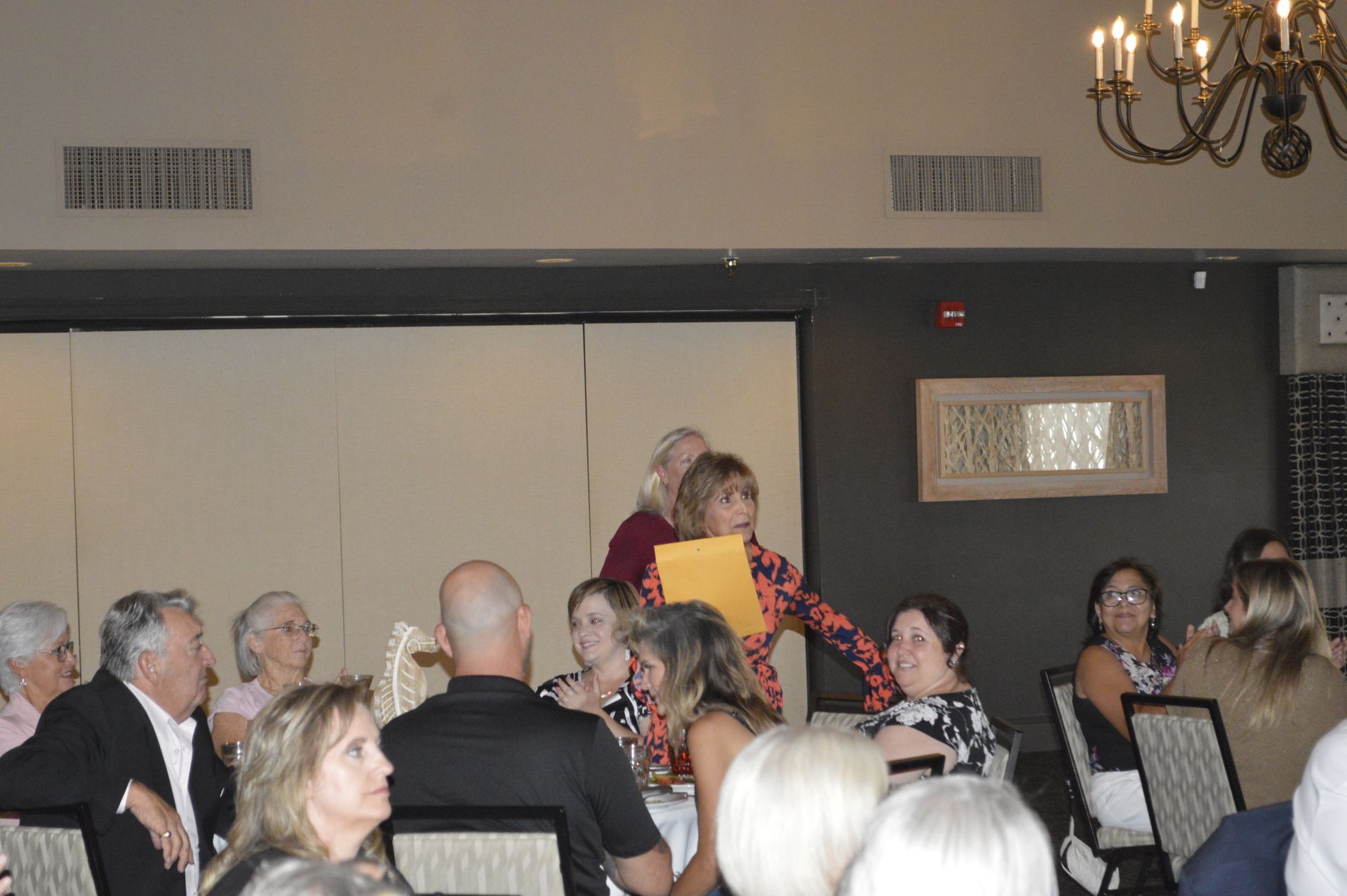 A group of people are sitting at tables in a room with a chandelier.