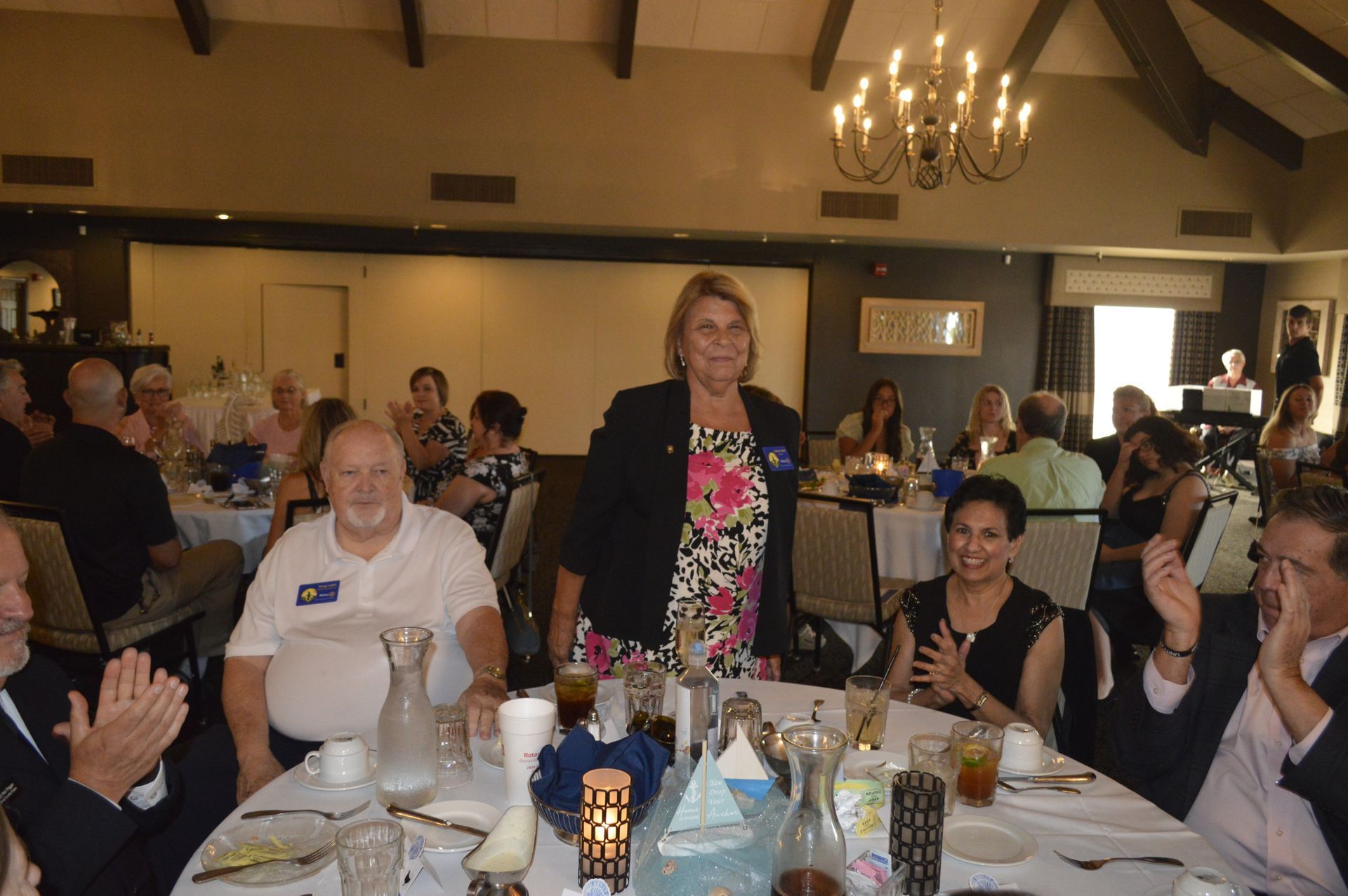 A woman is standing in front of a group of people sitting at tables in a restaurant.