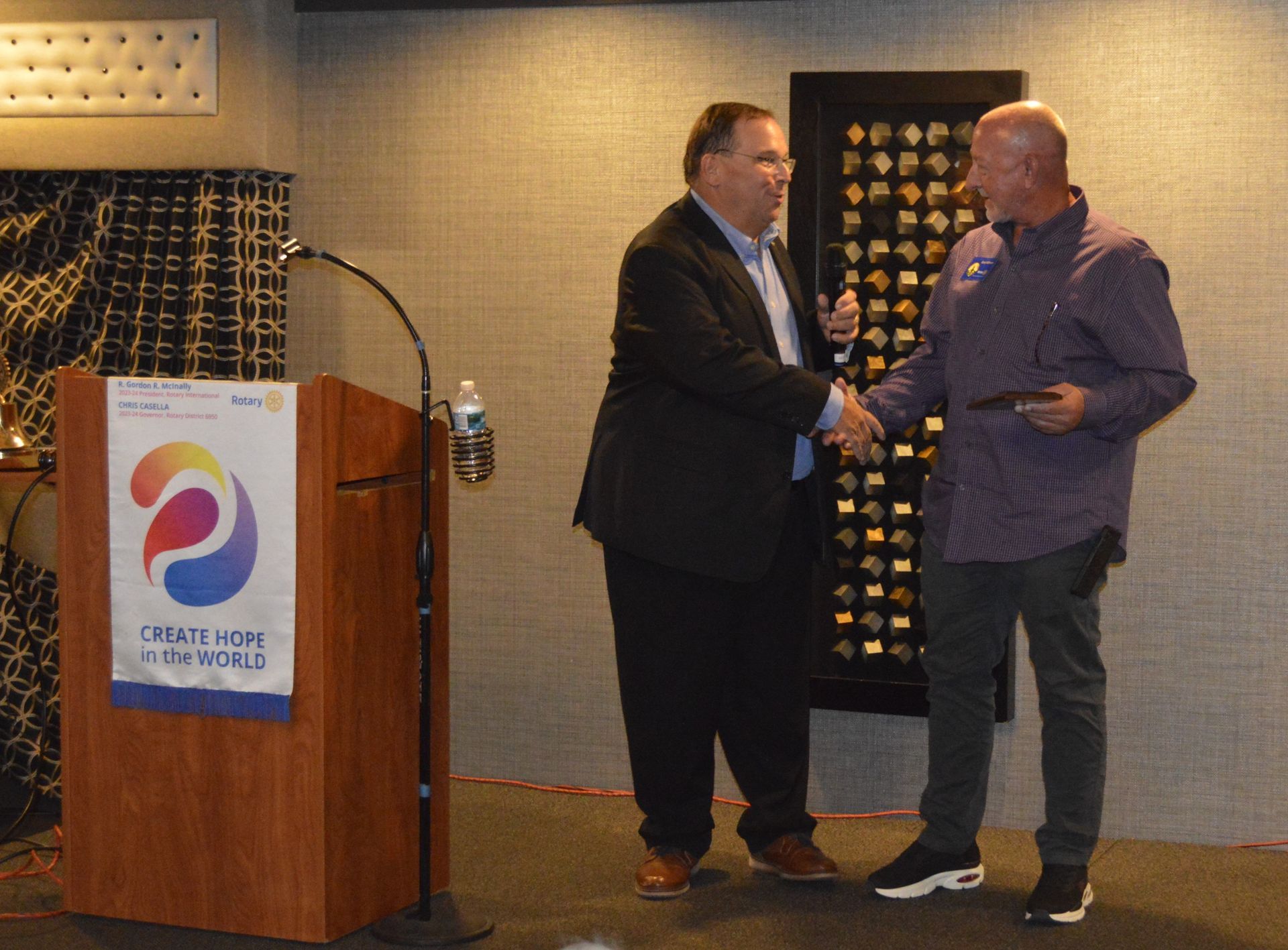 Two men shaking hands in front of a podium that says tribute for rivers