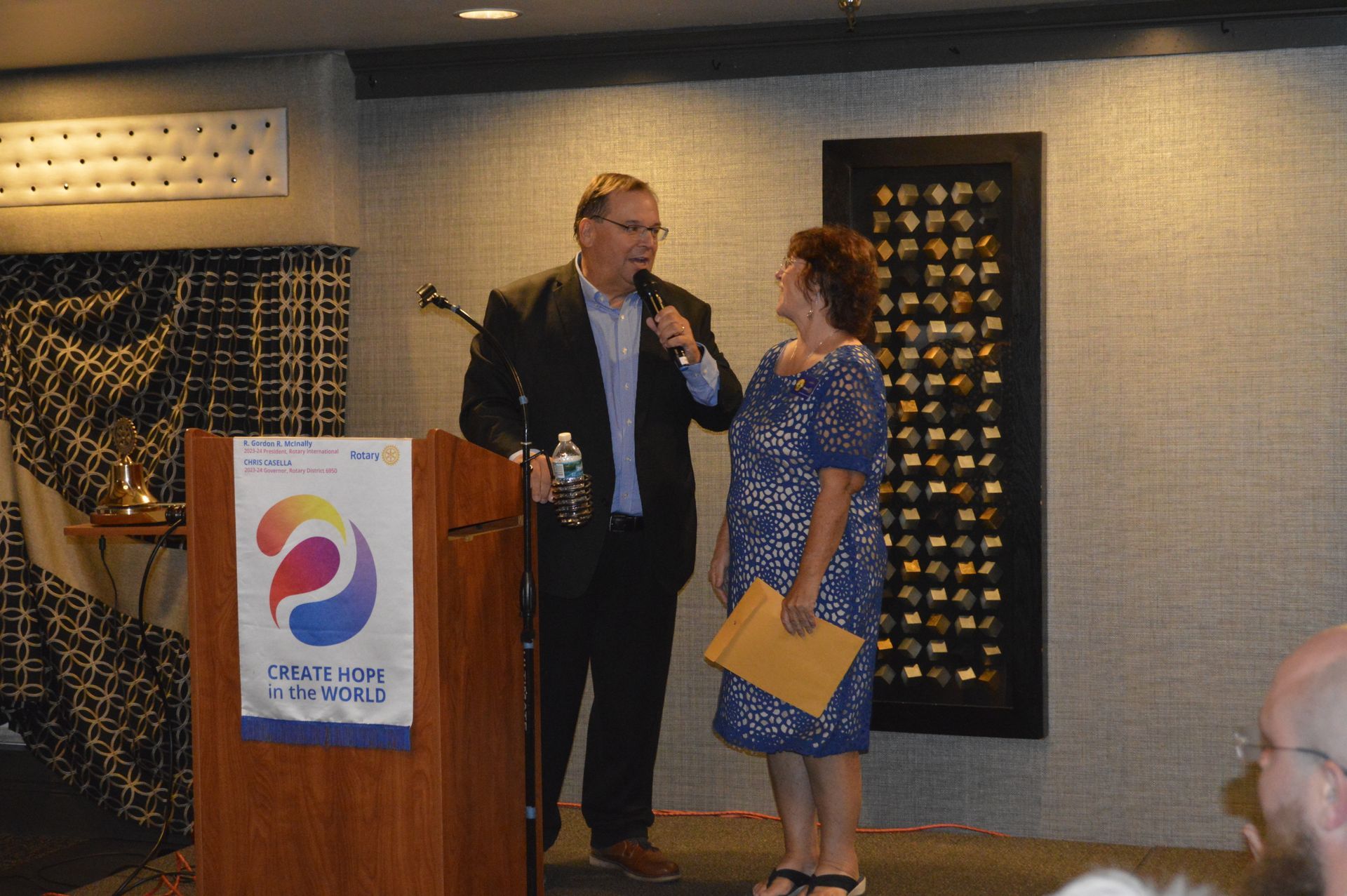 A man and a woman are standing in front of a podium talking into microphones.