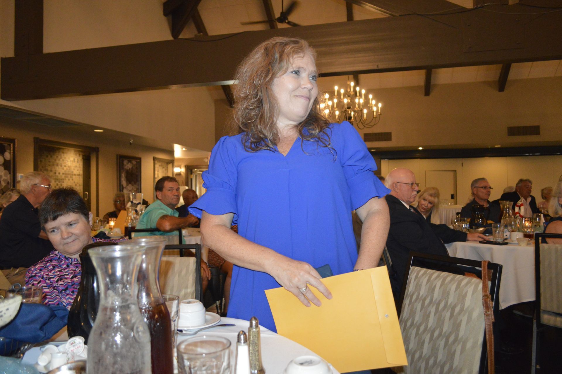 A woman in a blue dress is standing in a restaurant holding a yellow folder.