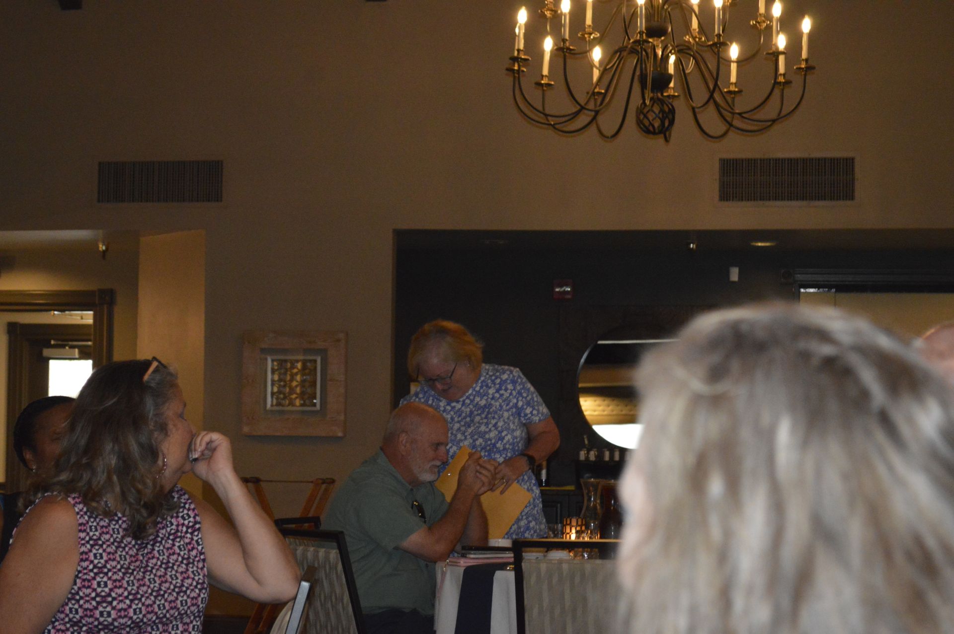 A group of people are sitting at a table in a room under a chandelier.
