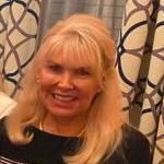 A woman with blonde hair is smiling in front of a curtain.