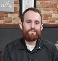A man with a beard is sitting in front of a brick wall.