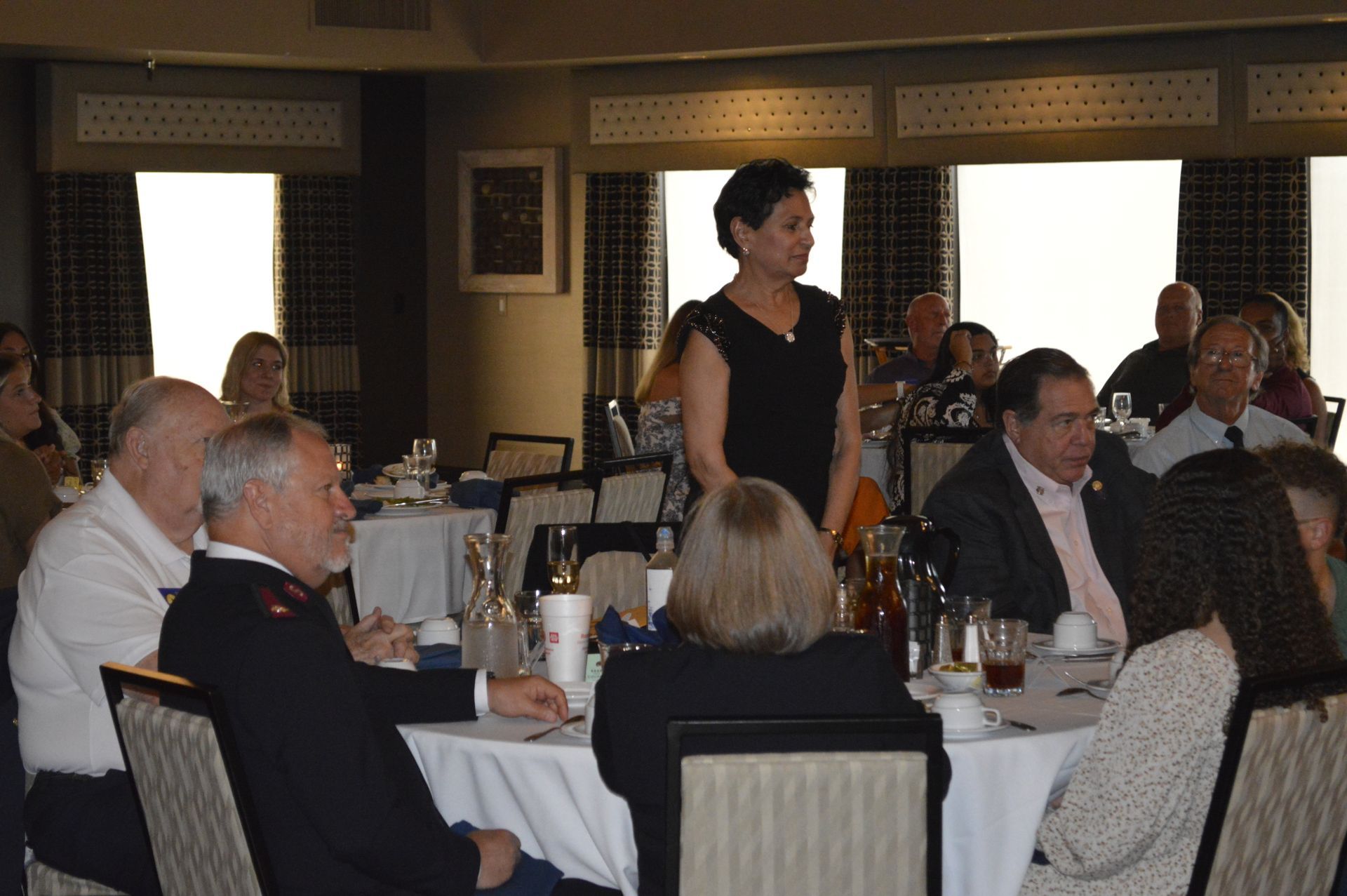 A woman is standing in front of a group of people sitting at tables.