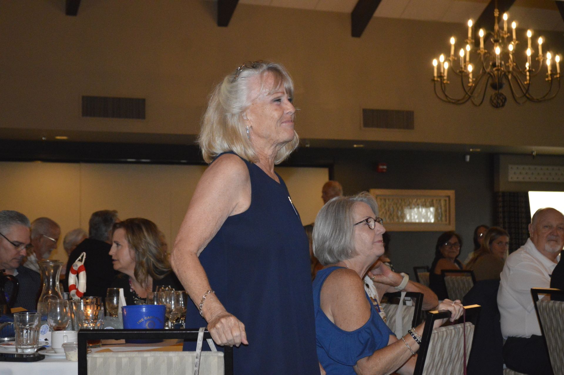 A woman in a blue dress is standing in a room with other people.