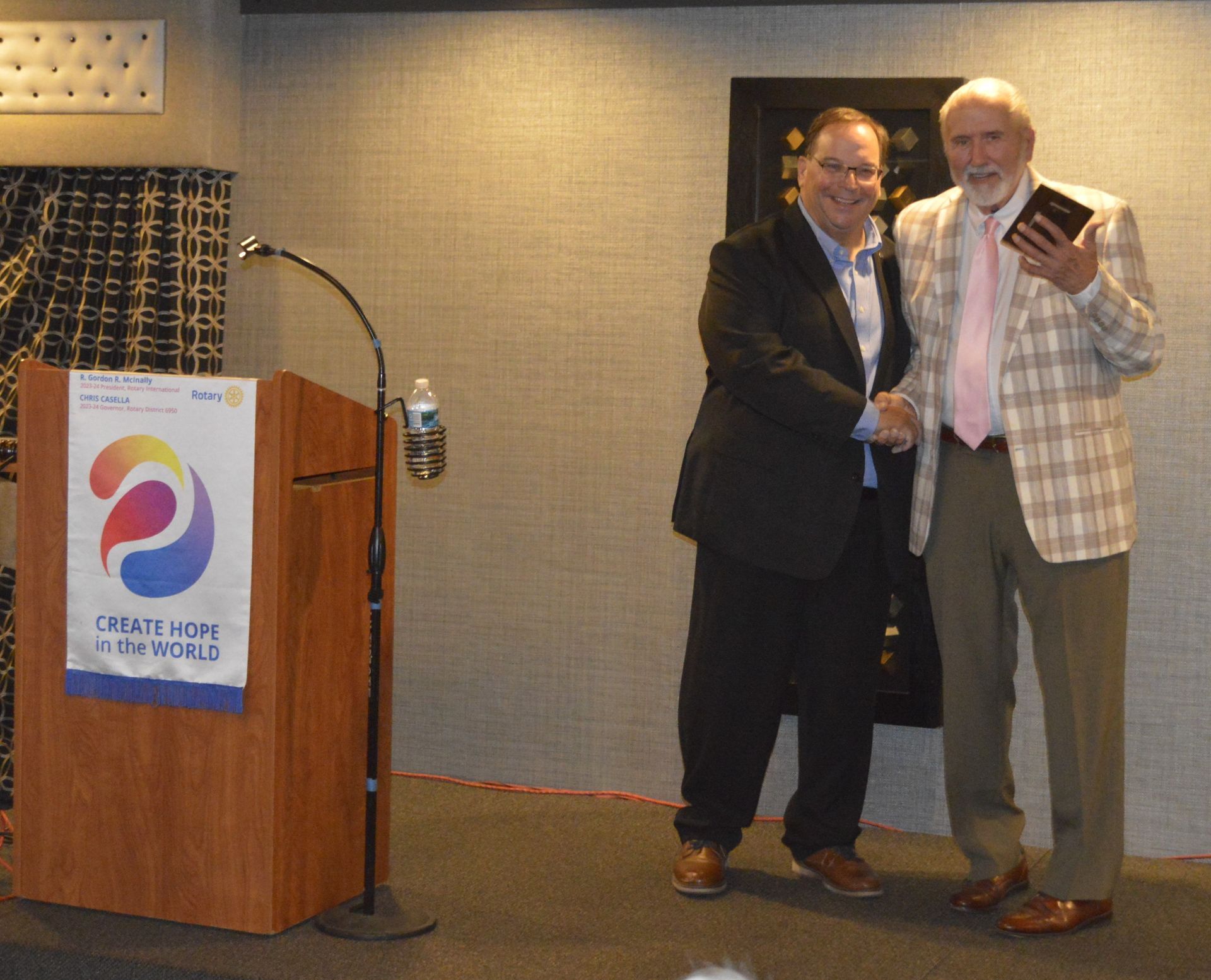 Two men shaking hands in front of a podium that says create for the world
