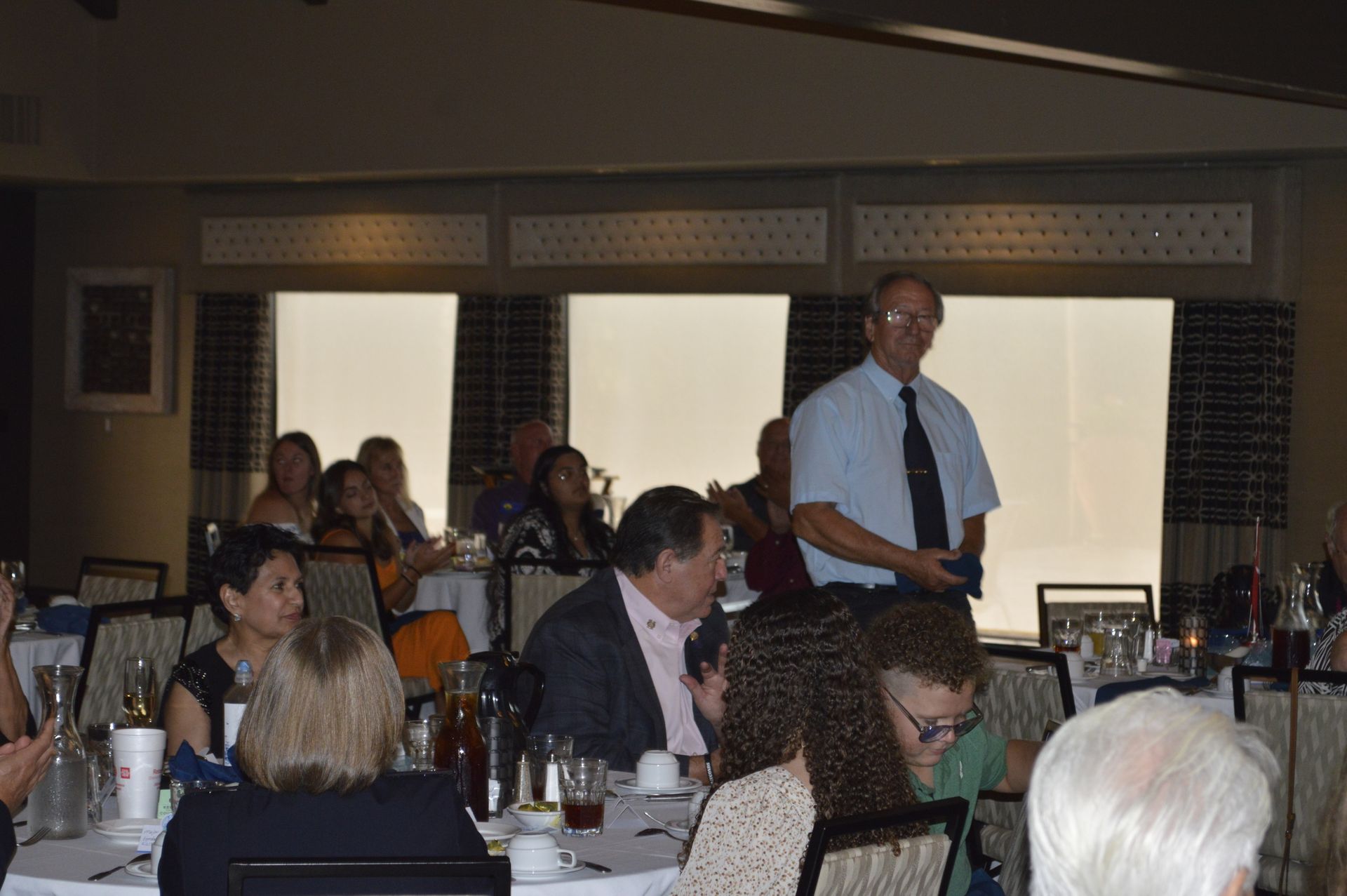 A man is standing in front of a group of people sitting at tables in a restaurant.