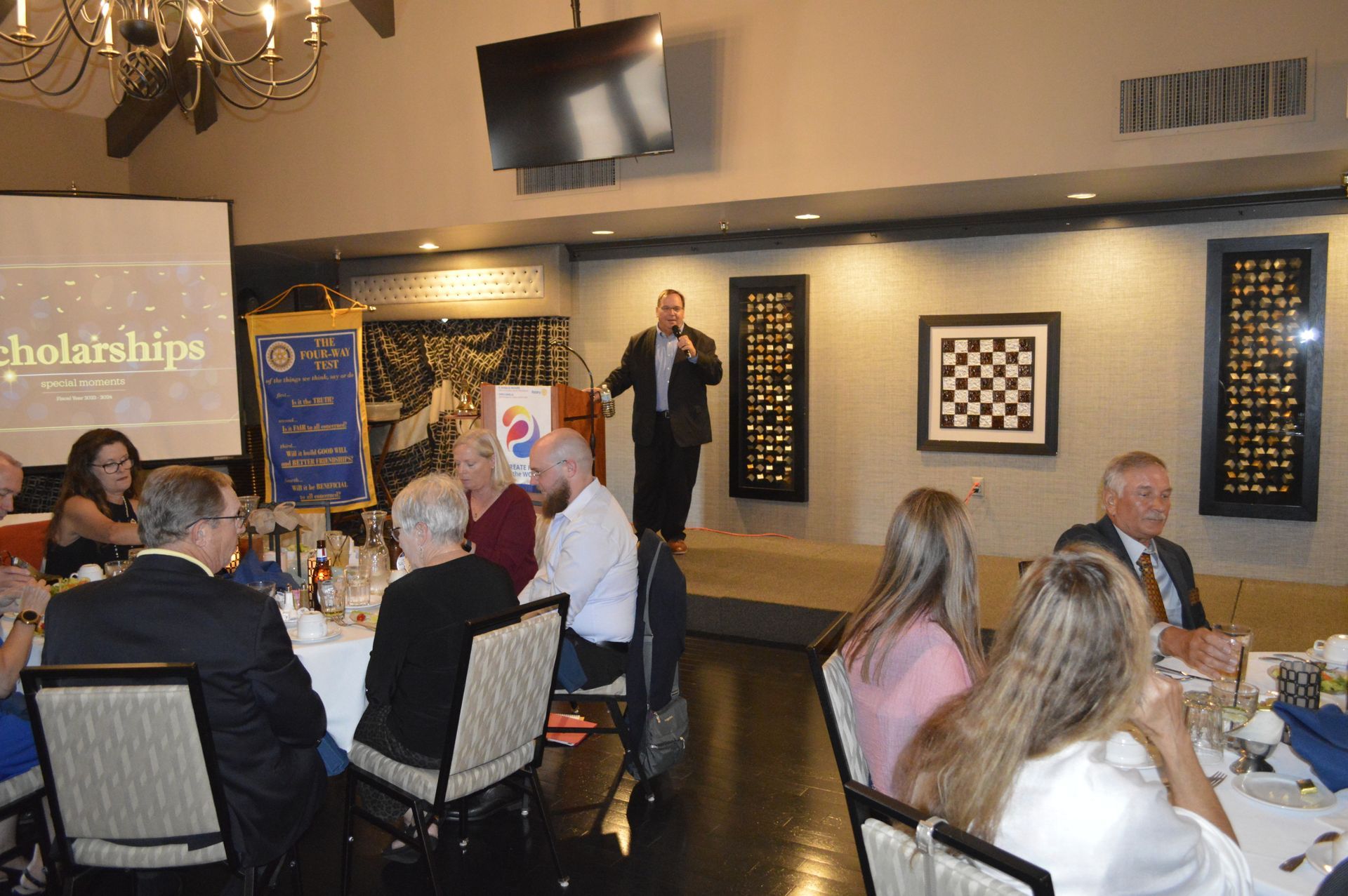 A man is standing at a podium giving a speech to a group of people sitting at tables.