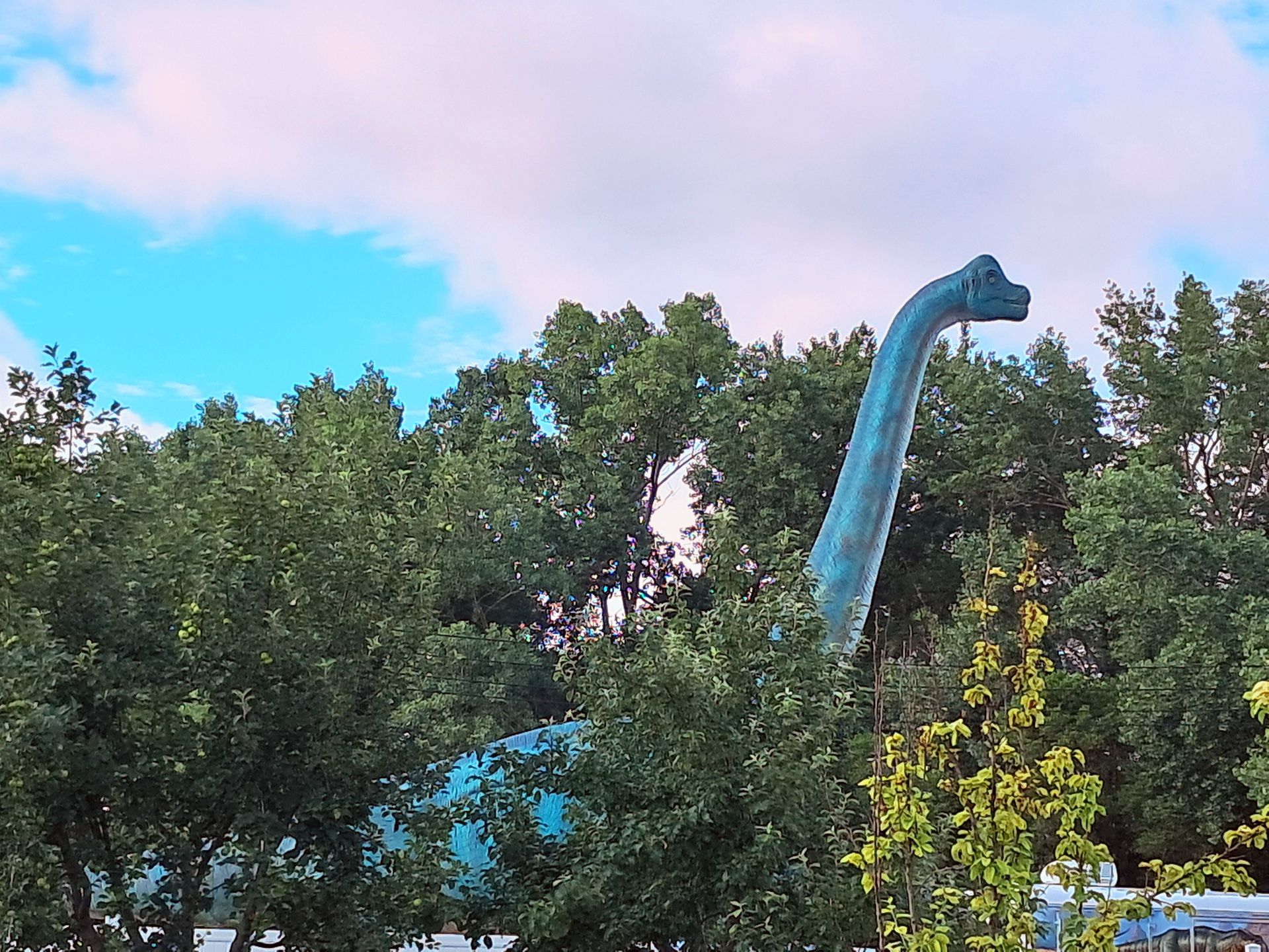 A large blue dinosaur statue is surrounded by trees.