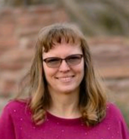 A woman wearing glasses and a pink sweater is smiling for the camera.