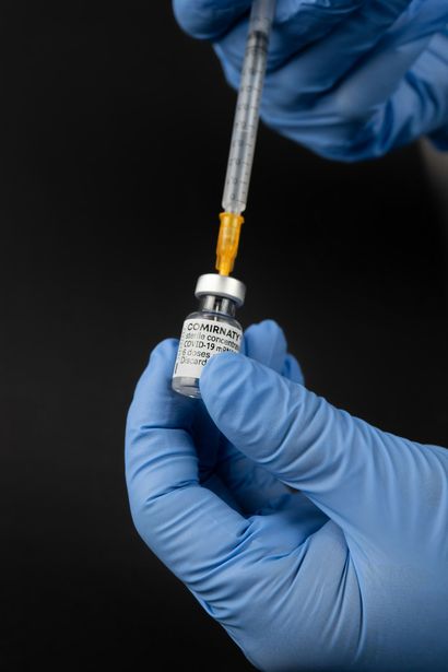 Gloved hands drawing liquid into a syringe from a small vial on a dark background