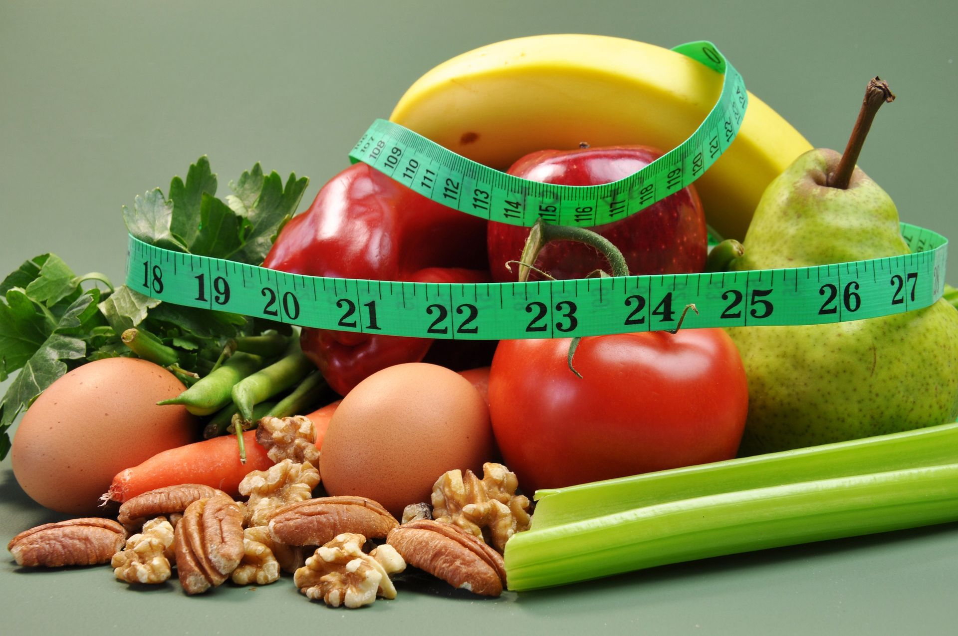 Assorted fresh fruits, vegetables, eggs, and nuts with a green measuring tape around them