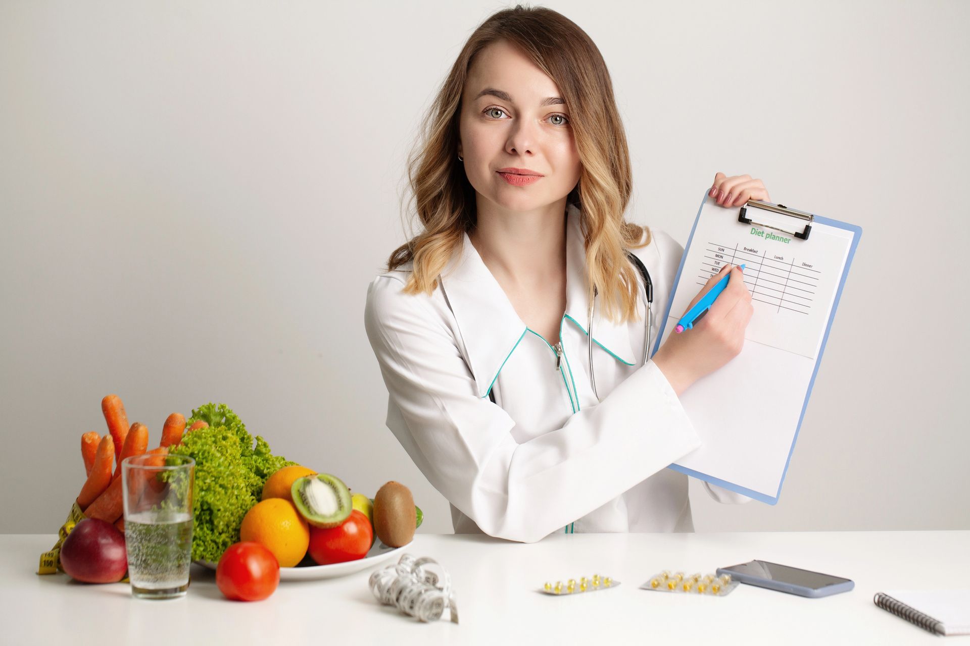 Nutritionist holding a clipboard beside fresh fruits, vegetables, and supplements on a white table