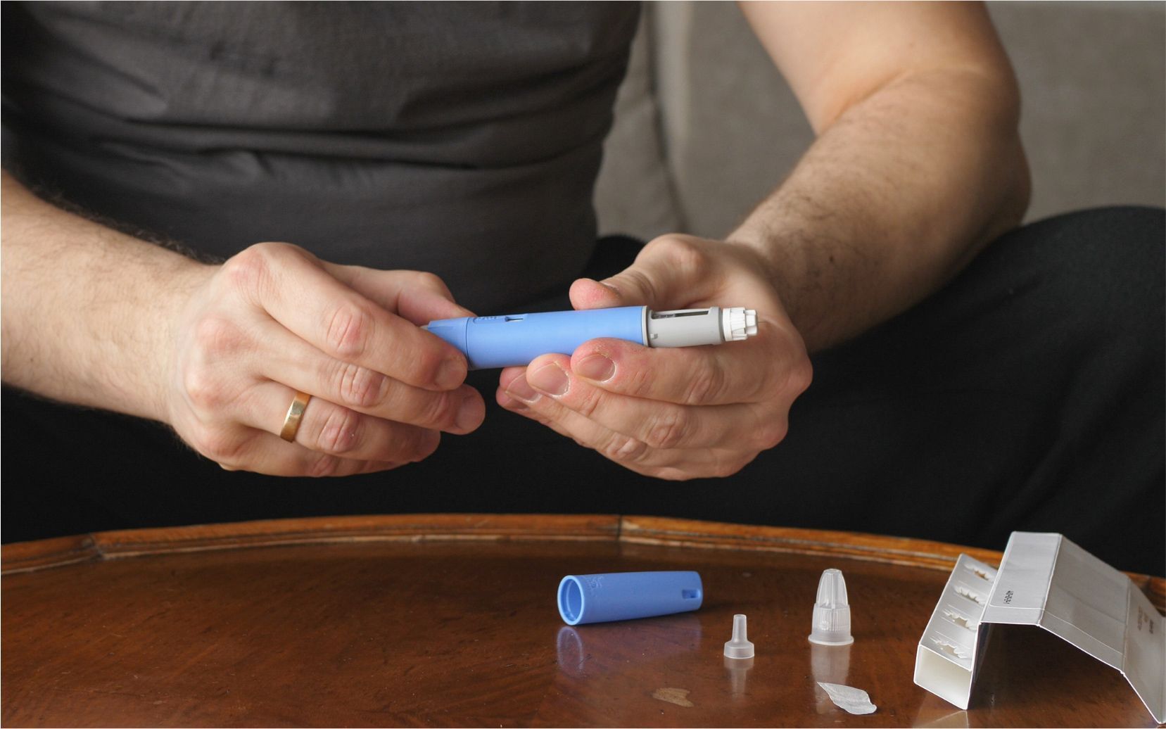 Hands holding a blue inhaler-like device above a table with small plastic parts and packaging pieces.