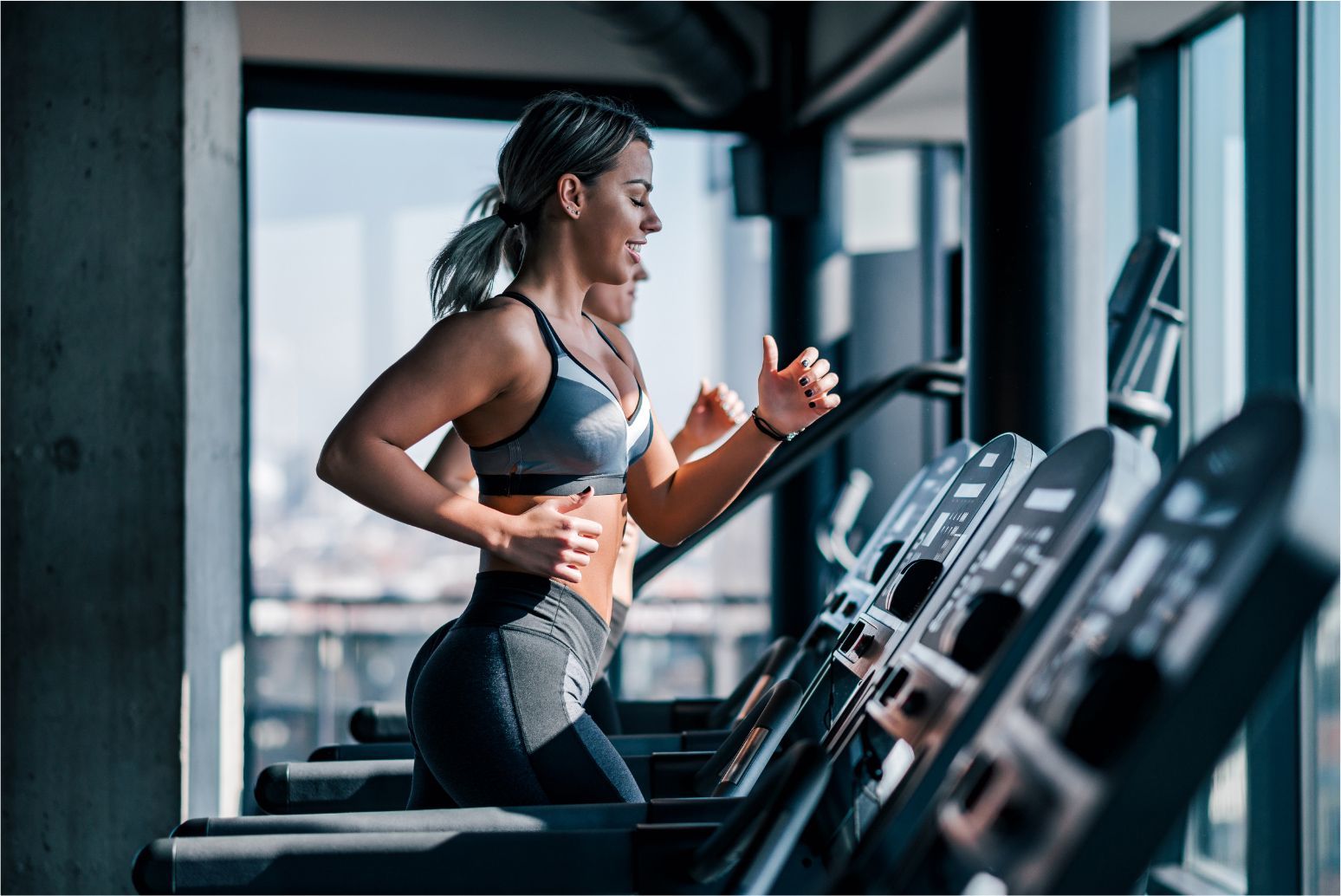 Woman running on a treadmill in a gym, wearing black workout clothes.