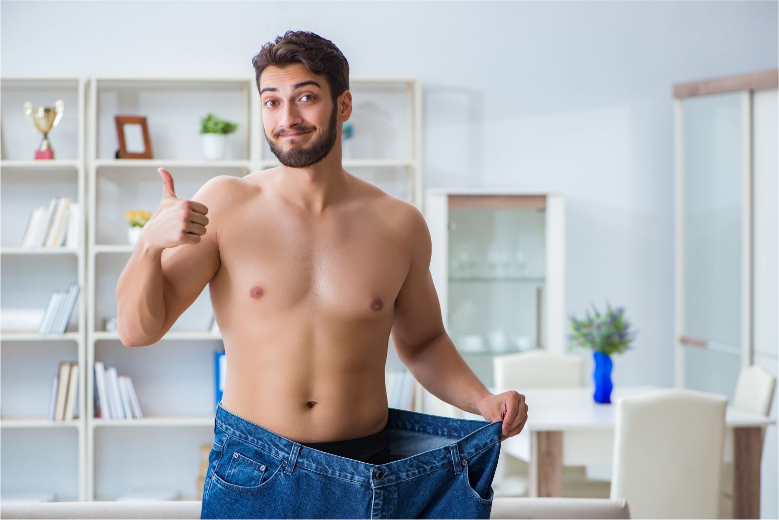 Man standing in a bright room, giving a thumbs-up while holding up oversized jeans