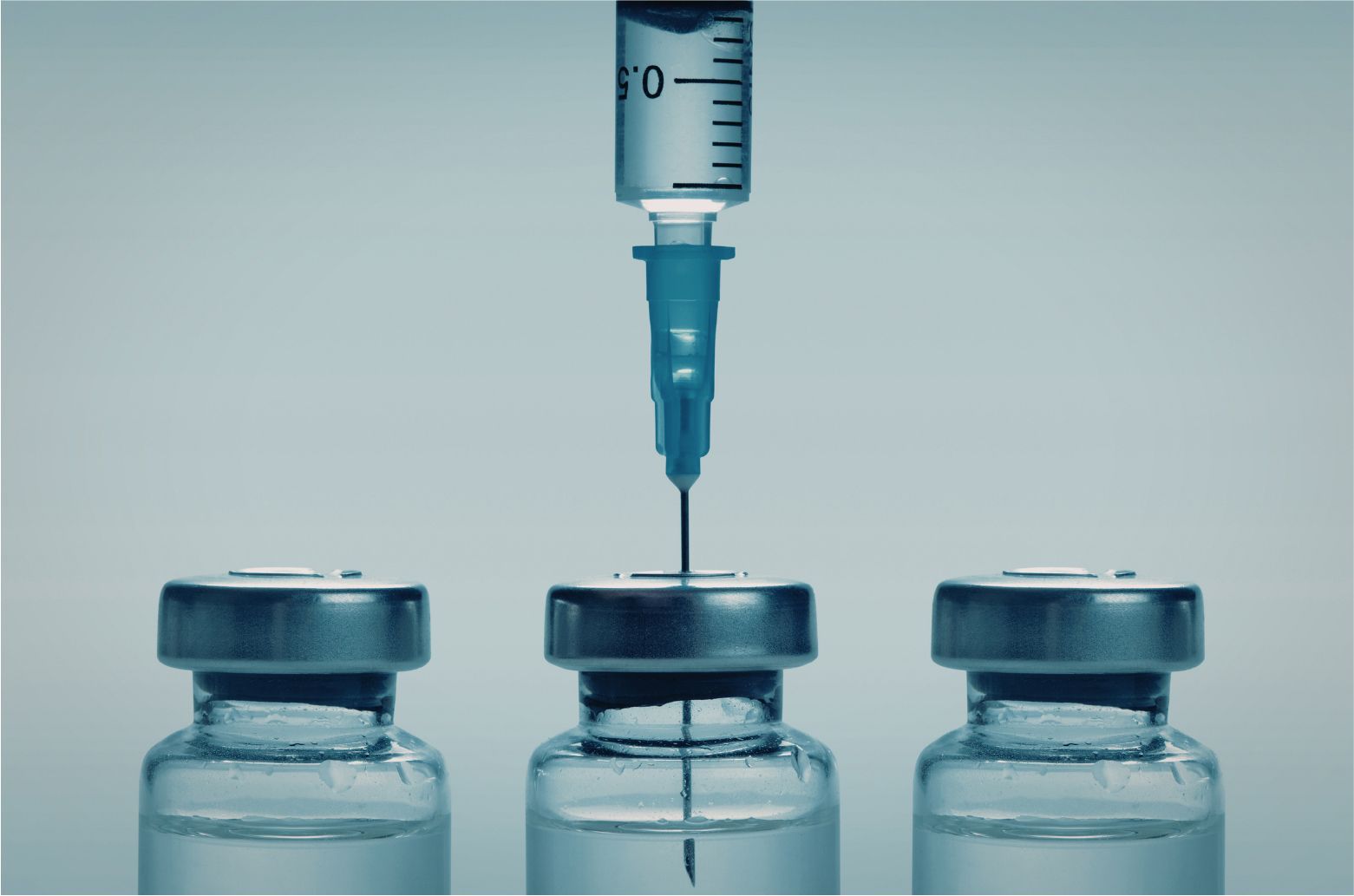 Syringe above three vaccine vials, one needle positioned over the center vial