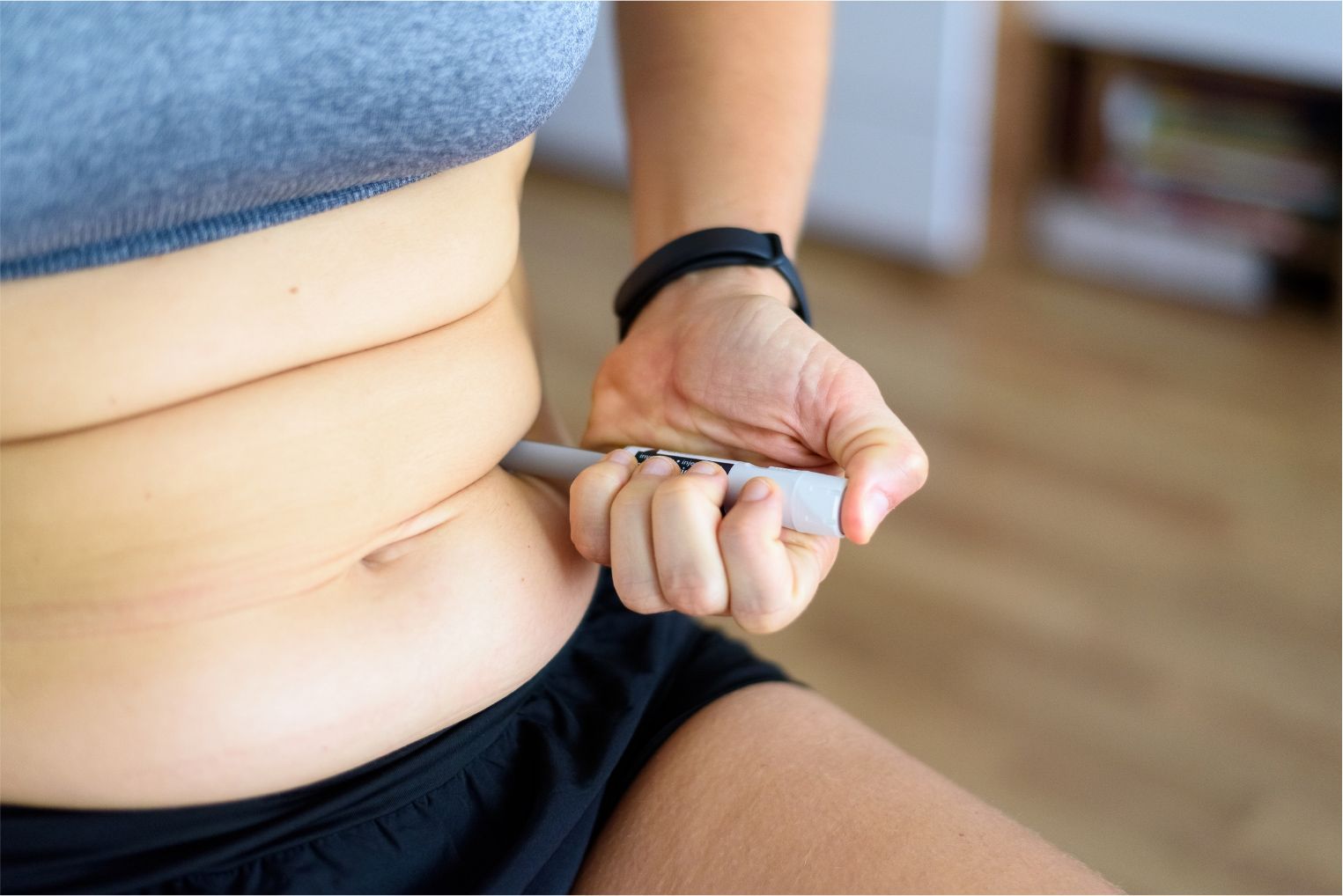 Close-up of a person pinching abdominal fat while seated, wearing a blue top and black shorts.