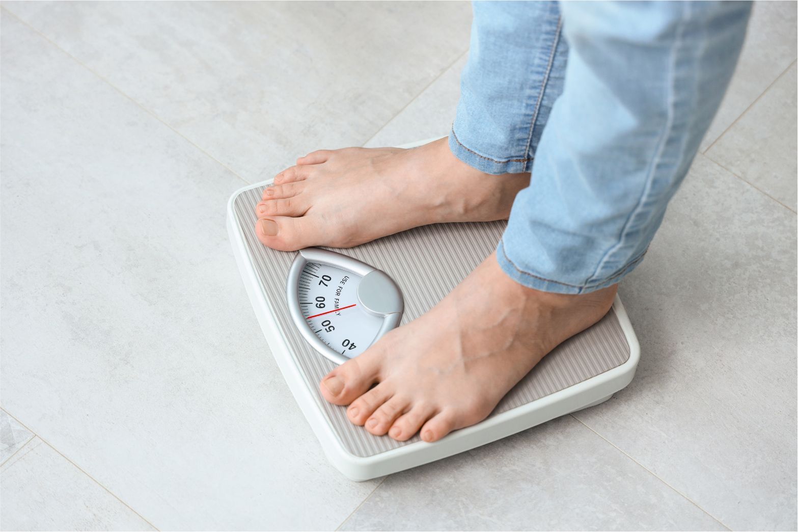 Feet on a bathroom scale measuring weight on a light tile floor
