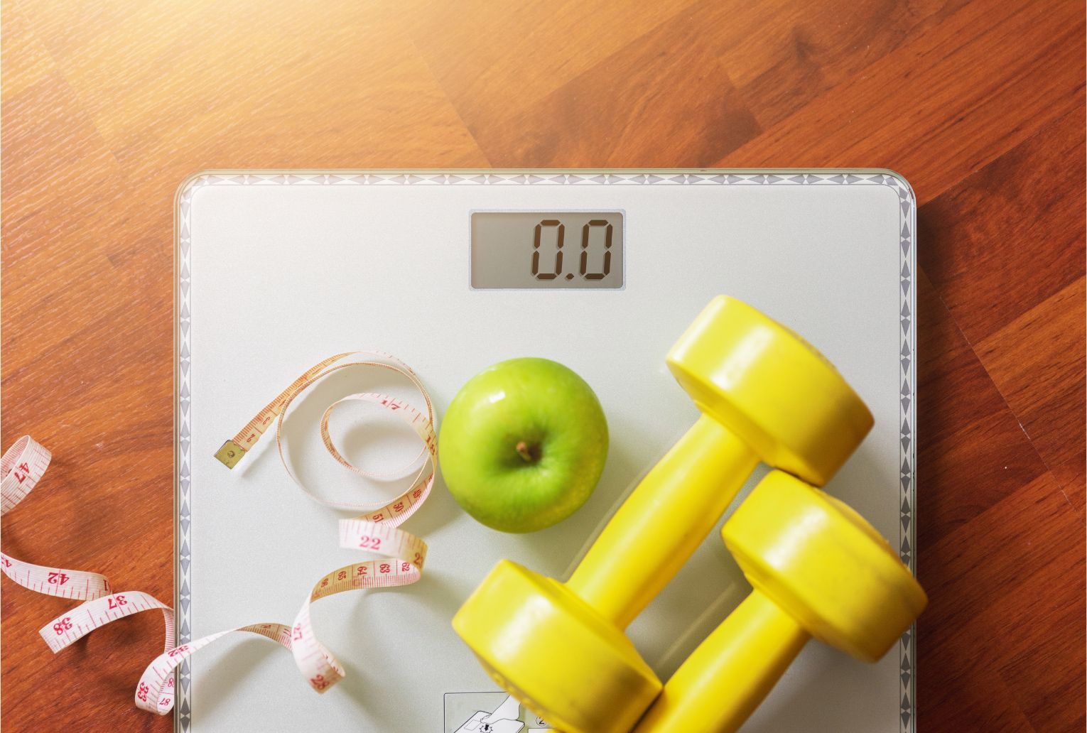 Green apple, yellow dumbbells, measuring tape, and digital scale on a wooden floor