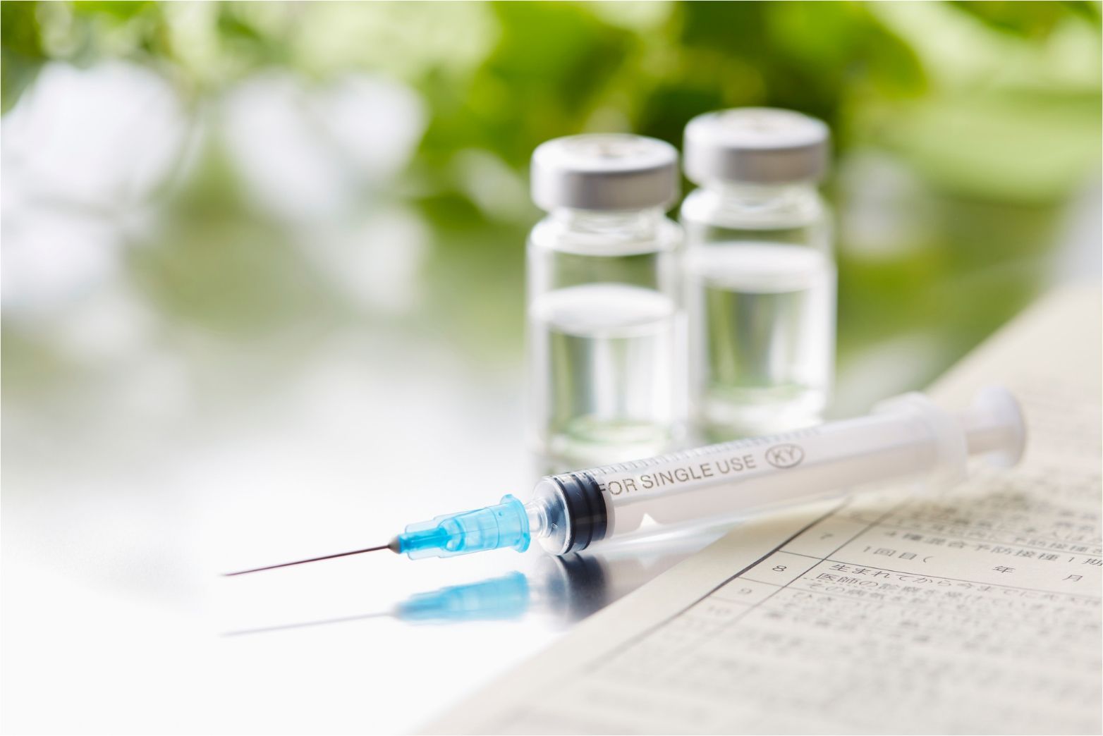 Syringe, medication vial, and two glass vials on a bright medical surface