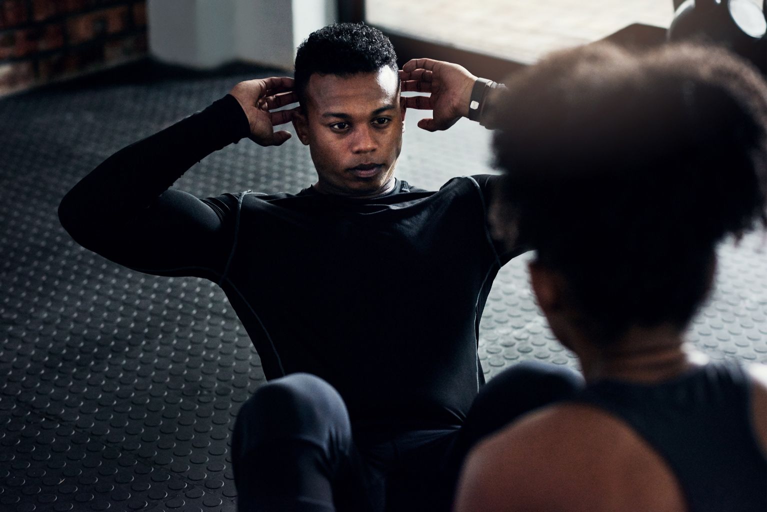 Person doing sit-ups indoors while another watches in the foreground
