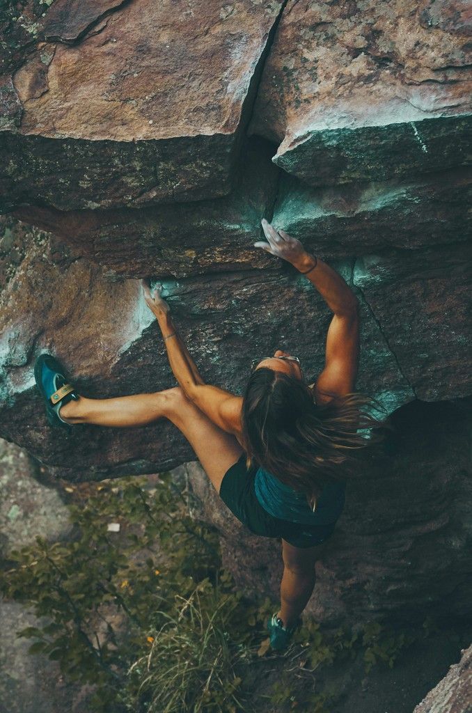 Rock climber reaching for a hold on a steep, mossy cliff face.