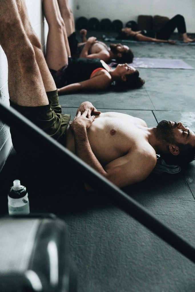 People lying on yoga mats in a dim studio, resting in a relaxation pose.