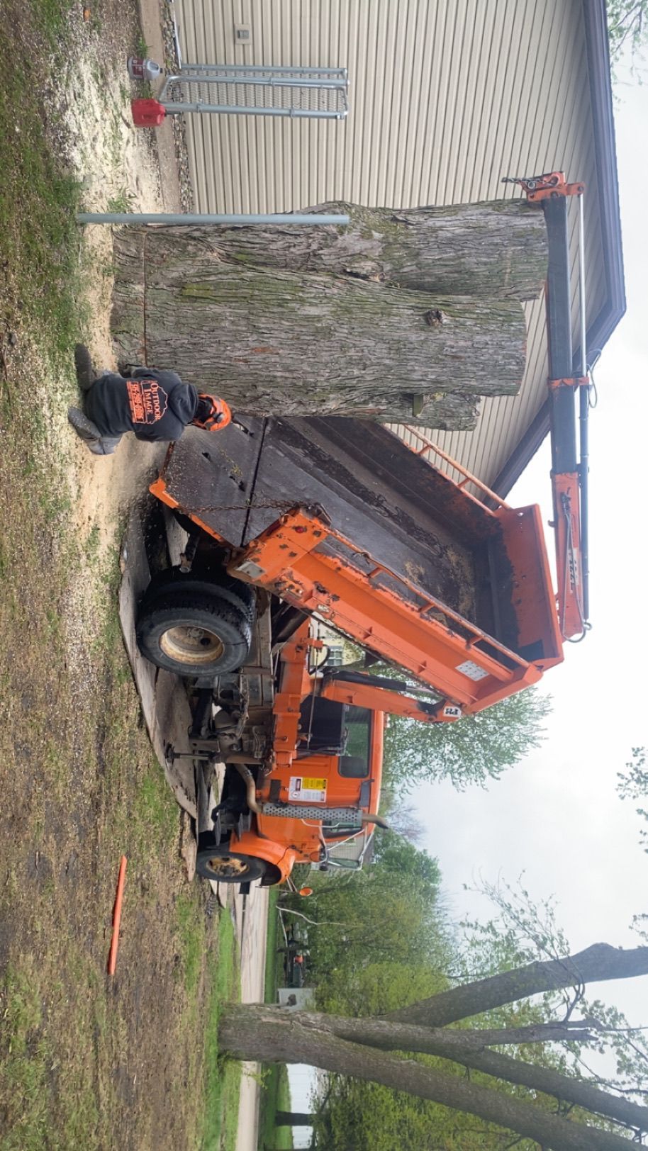 Orange dump truck parked in a yard, with debris and a striped garage wall in the background.