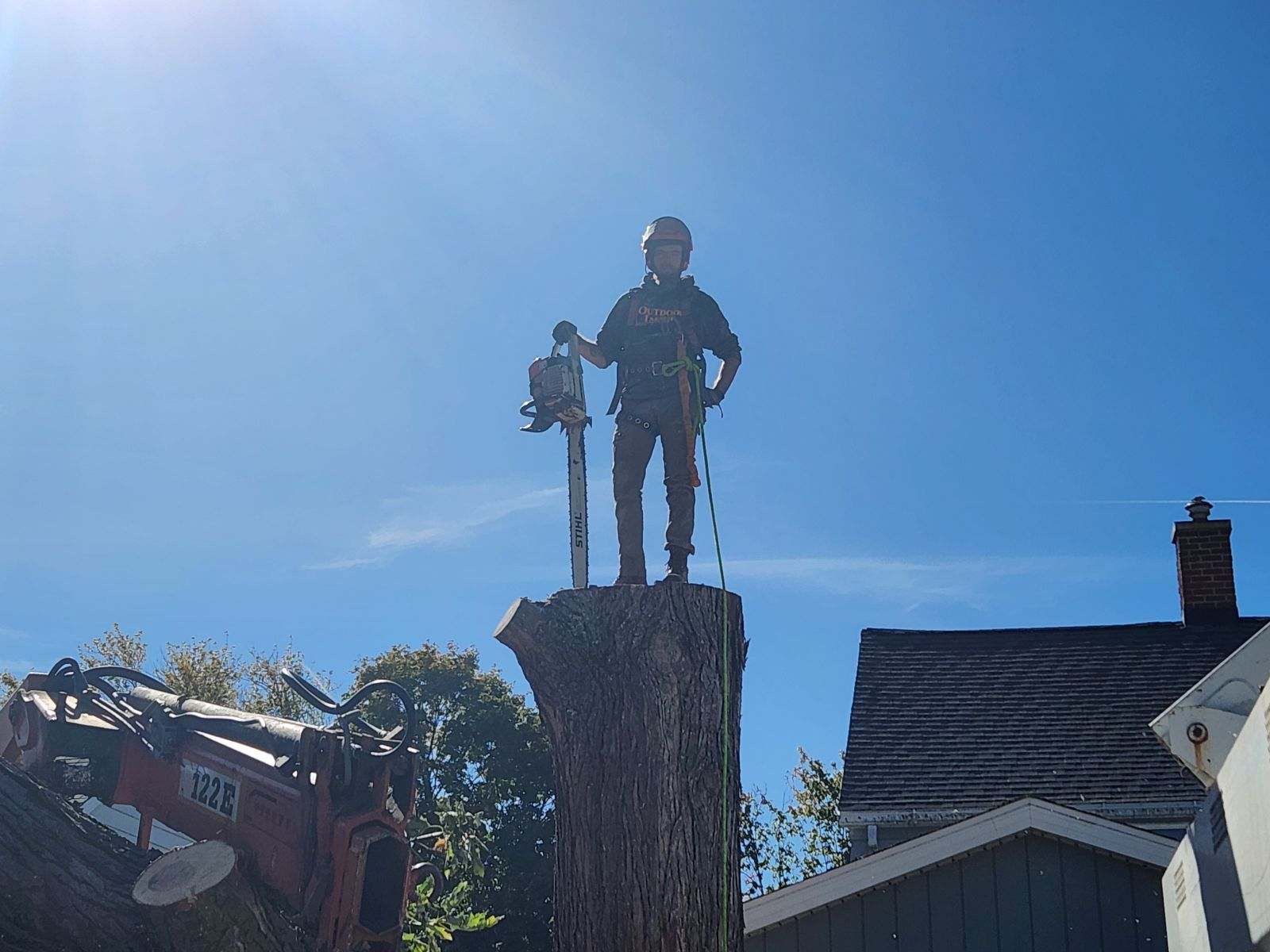 Statue of a person holding a tool atop a tall cut tree stump against a bright blue sky