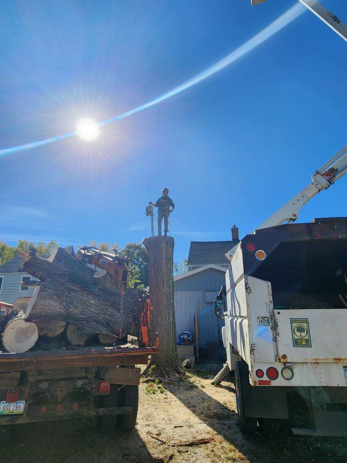 Two trucks on a sunny job site with a tall brick chimney and a person standing on top