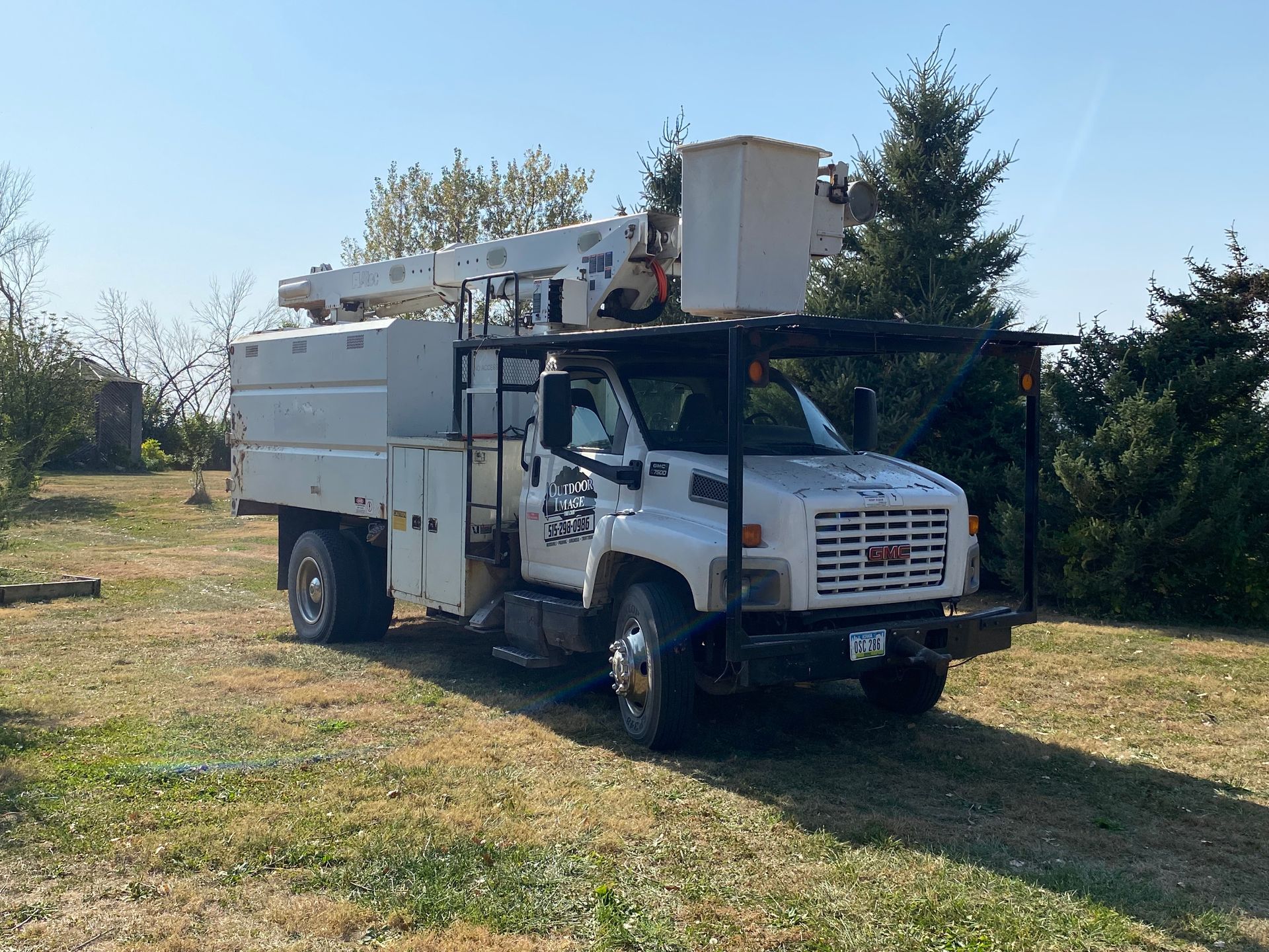 White utility bucket truck parked on grass in a sunny field with trees in the background