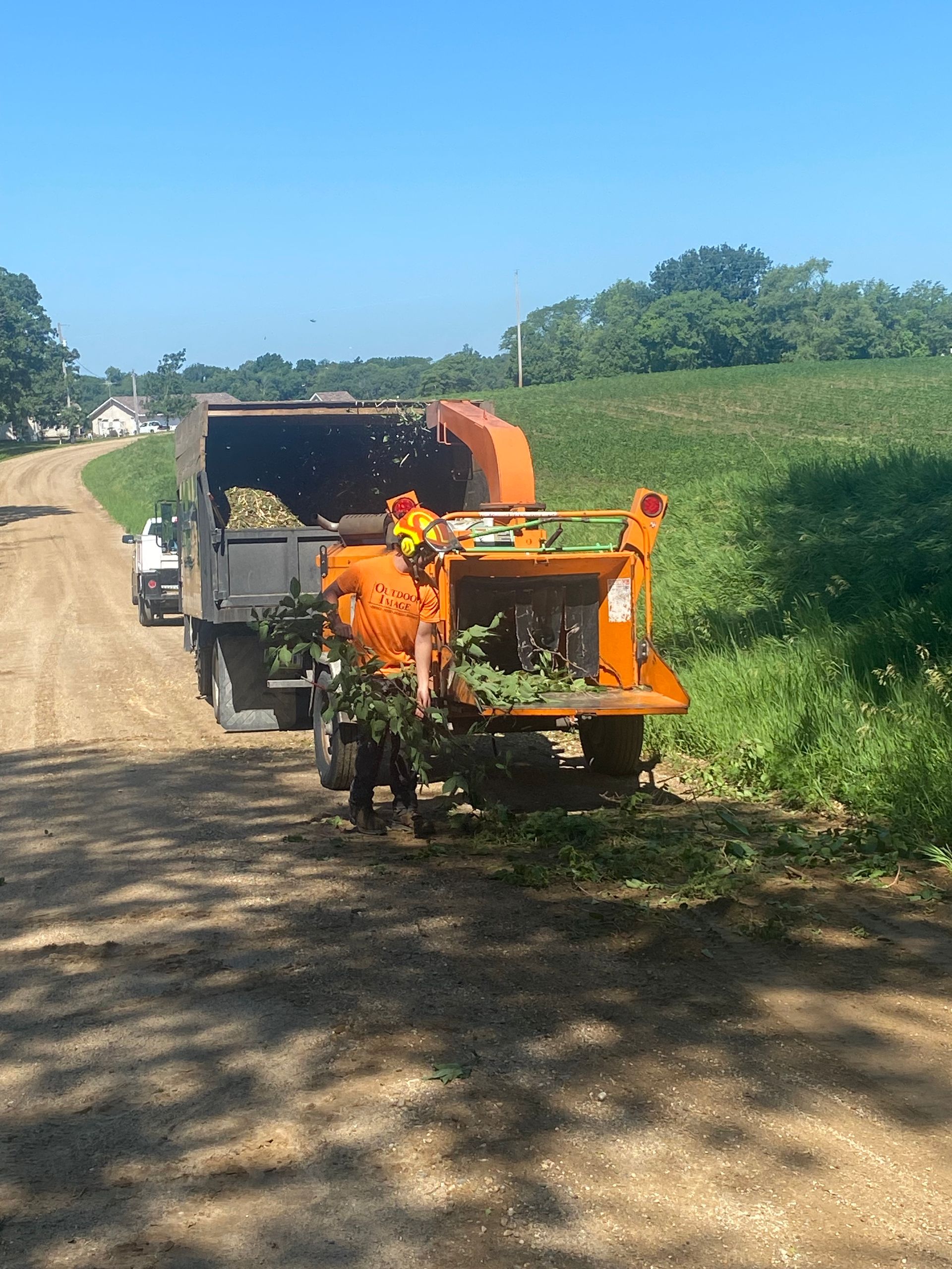 Orange farm machine on a dirt road beside green fields under a clear blue sky
