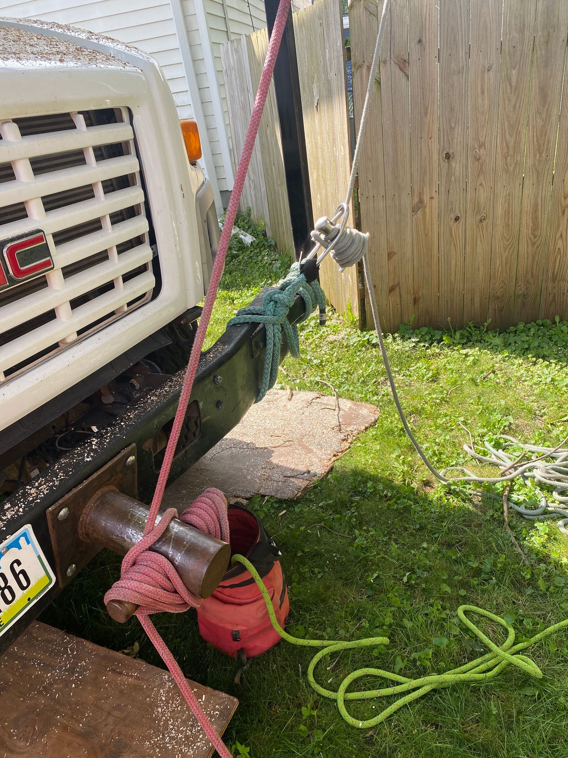 Bright green garden hose tangled near a parked truck and red bucket beside a fence and grassy yard