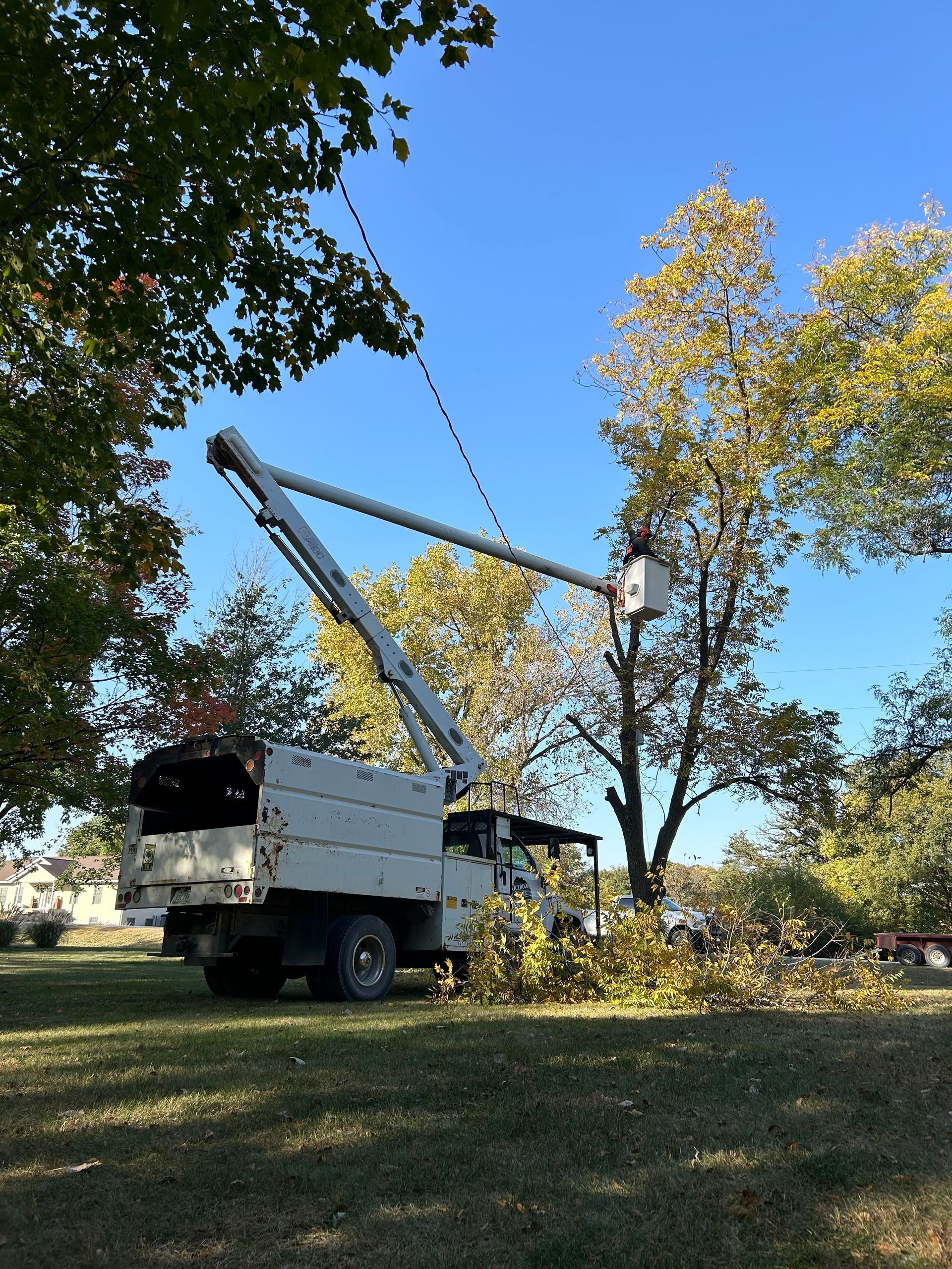 Truck-mounted bucket lift in a grassy yard under trees on a sunny day