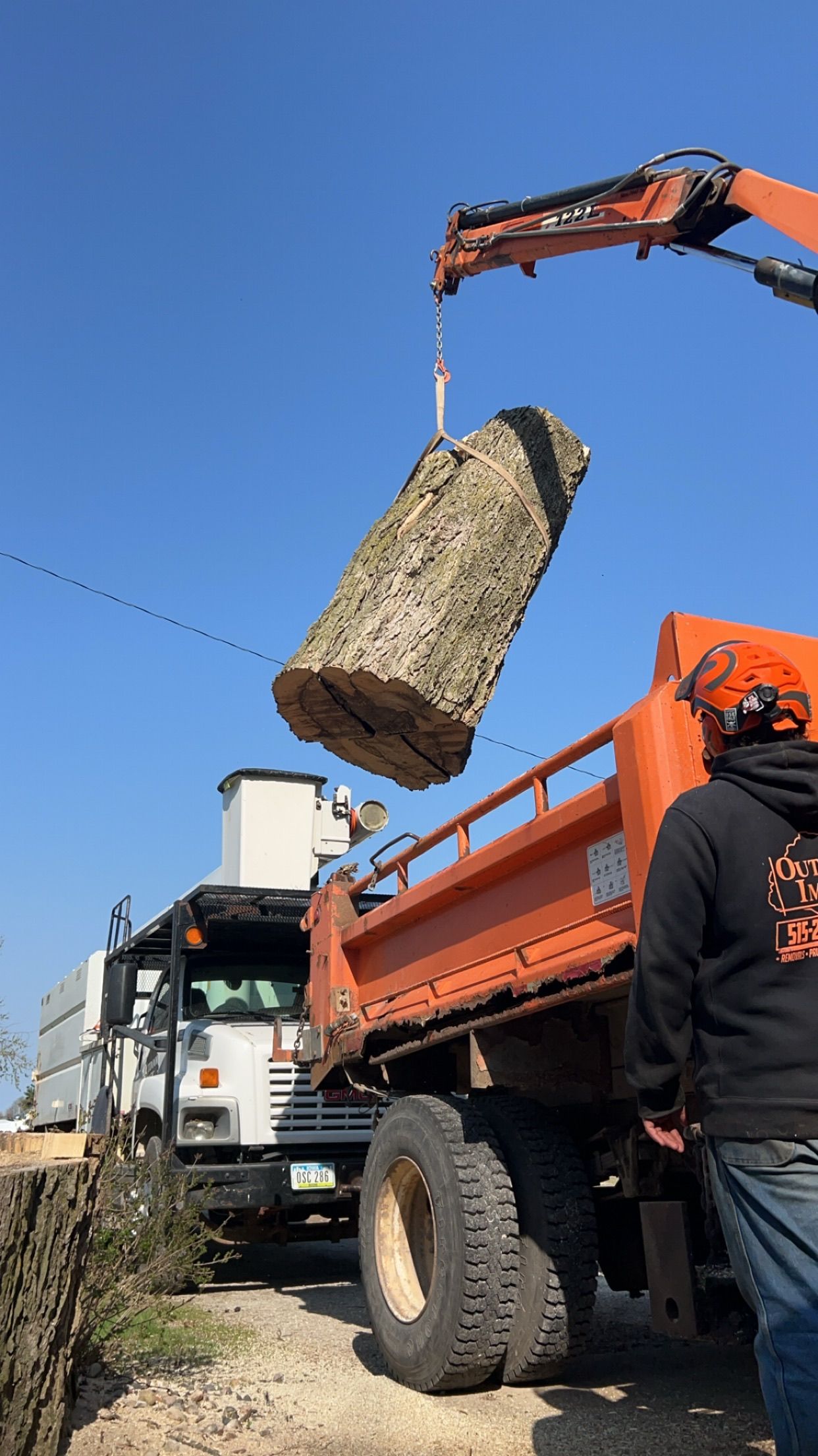 Orange crane lifting a large rock over a dump truck at a construction site.