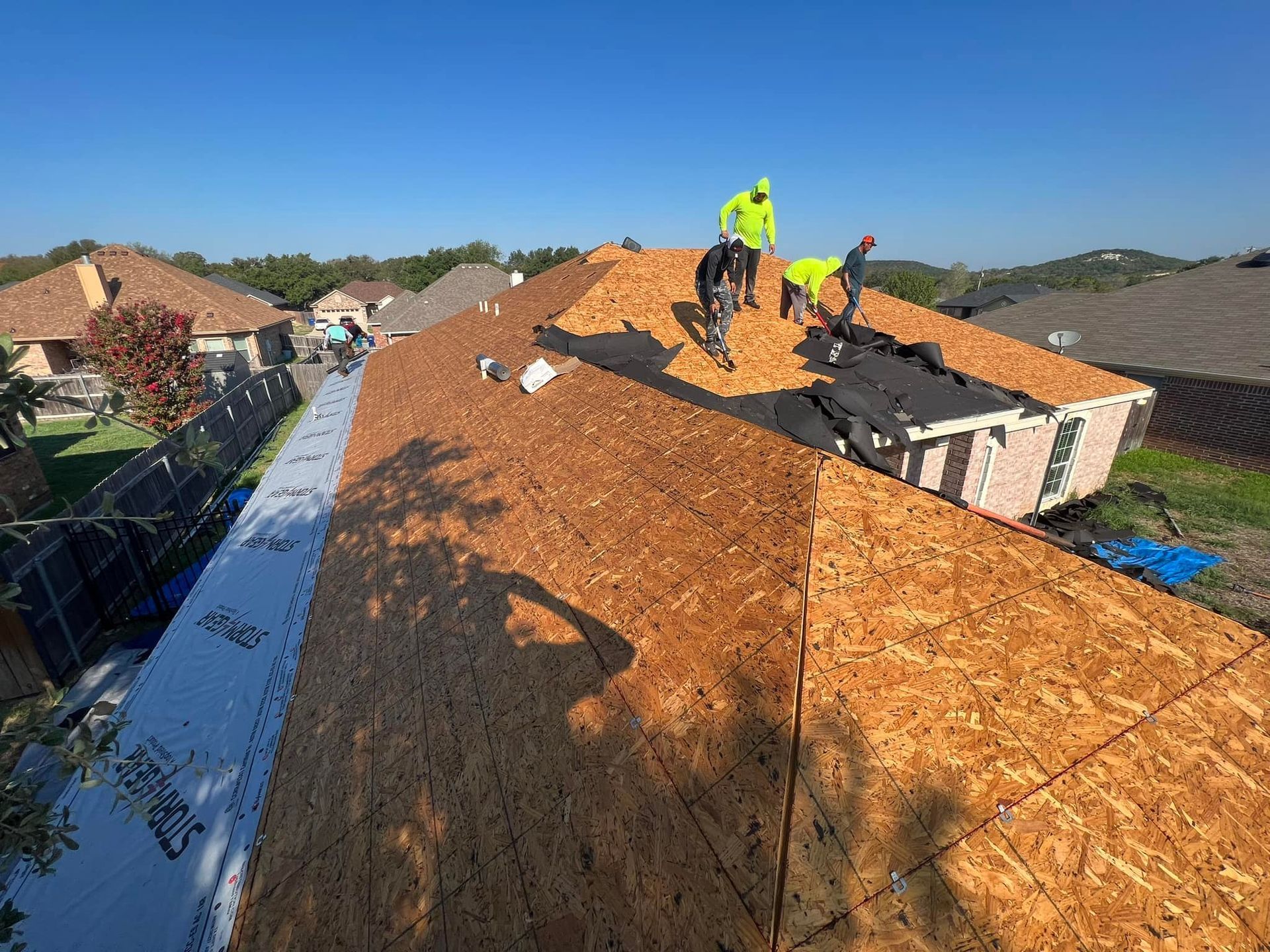 Roofers installing shingles on a house roof on a sunny day.