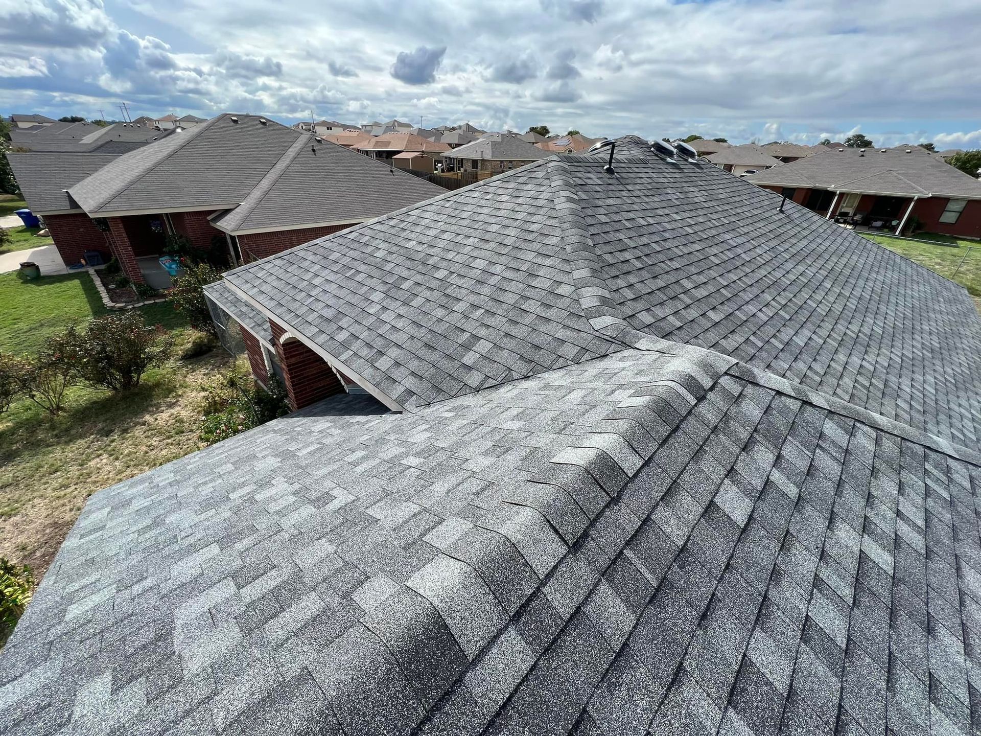 Gray shingle roofs of houses under cloudy sky; neighborhood view.