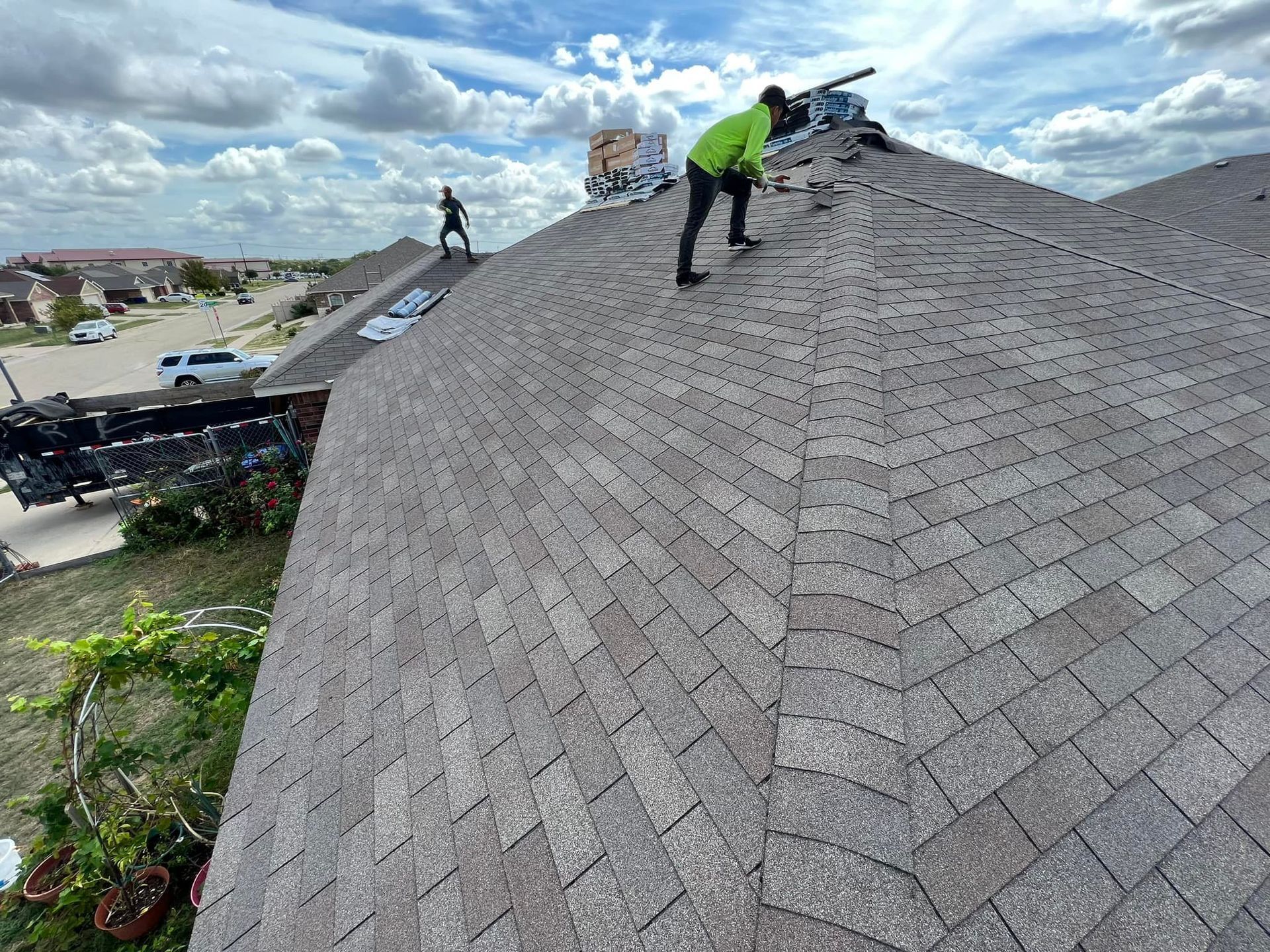 Two workers on a brown shingle roof, repairing shingles on a sunny day.