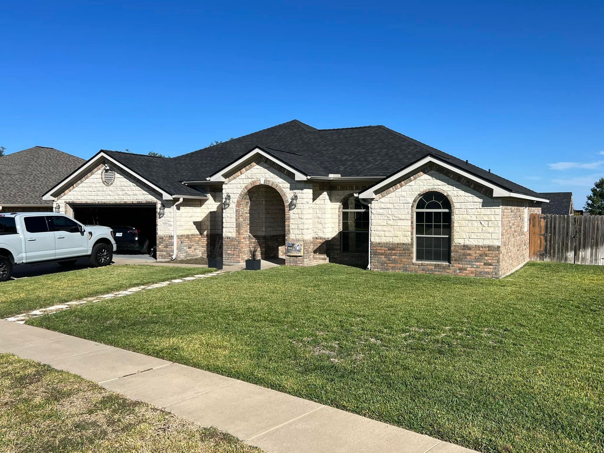 Beige brick house with dark roof, arched entryway, and attached garage on a grassy lawn.