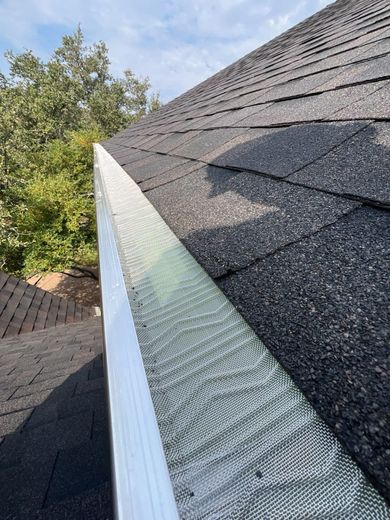Close-up of a roof with black shingles and a gutter with a silver screen.