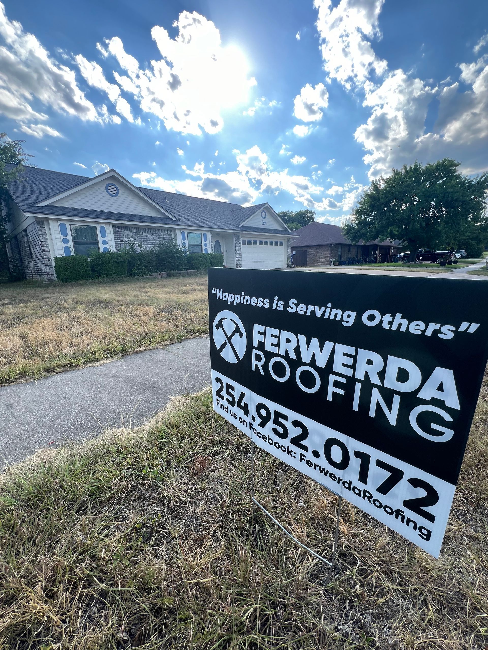 Ferwerda Roofing sign in front of a house, sunny sky with clouds.