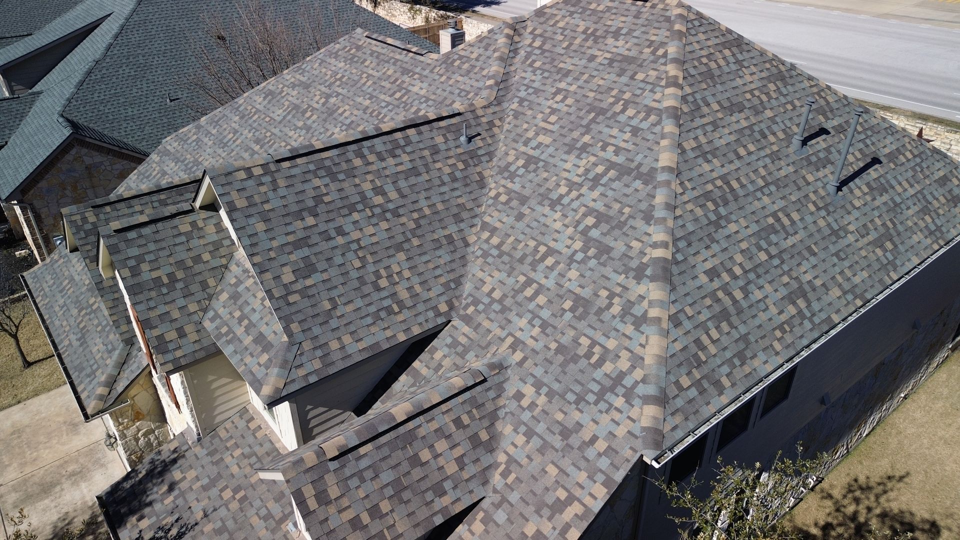 A complex roof with dark asphalt shingles, varying shades of gray and brown, on a residential house.
