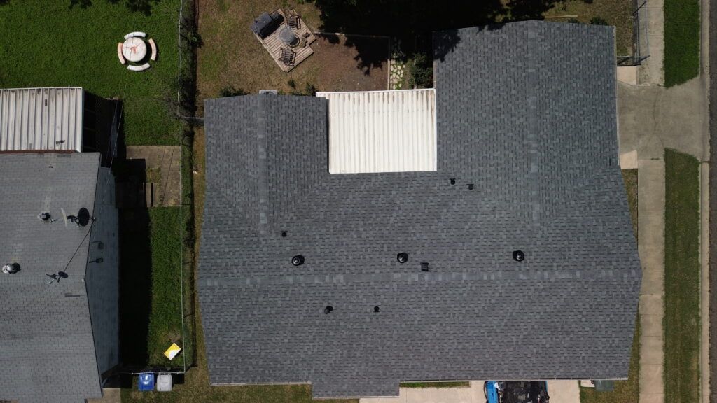Overhead view of a dark gray shingled roof with a white rectangular section and several vents.