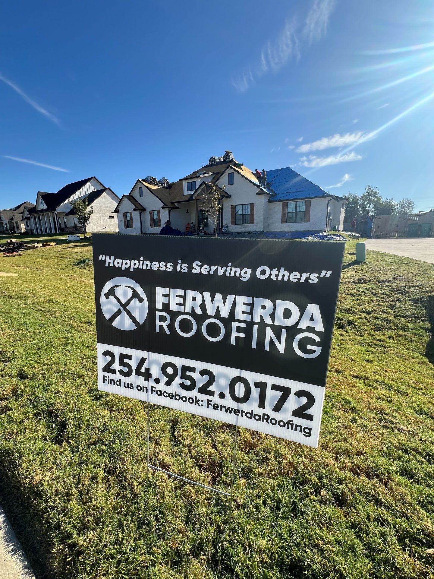 Sign for Ferwerda Roofing with a house under construction in the background. The sign has a phone number and says 