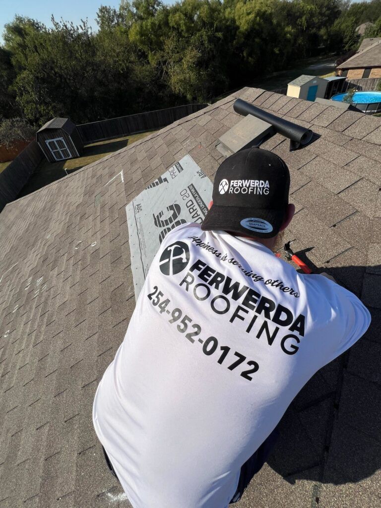 Roofer on a roof installing flashing. Company logo on shirt. Phone number 254-952-0172. Outdoors, daytime.
